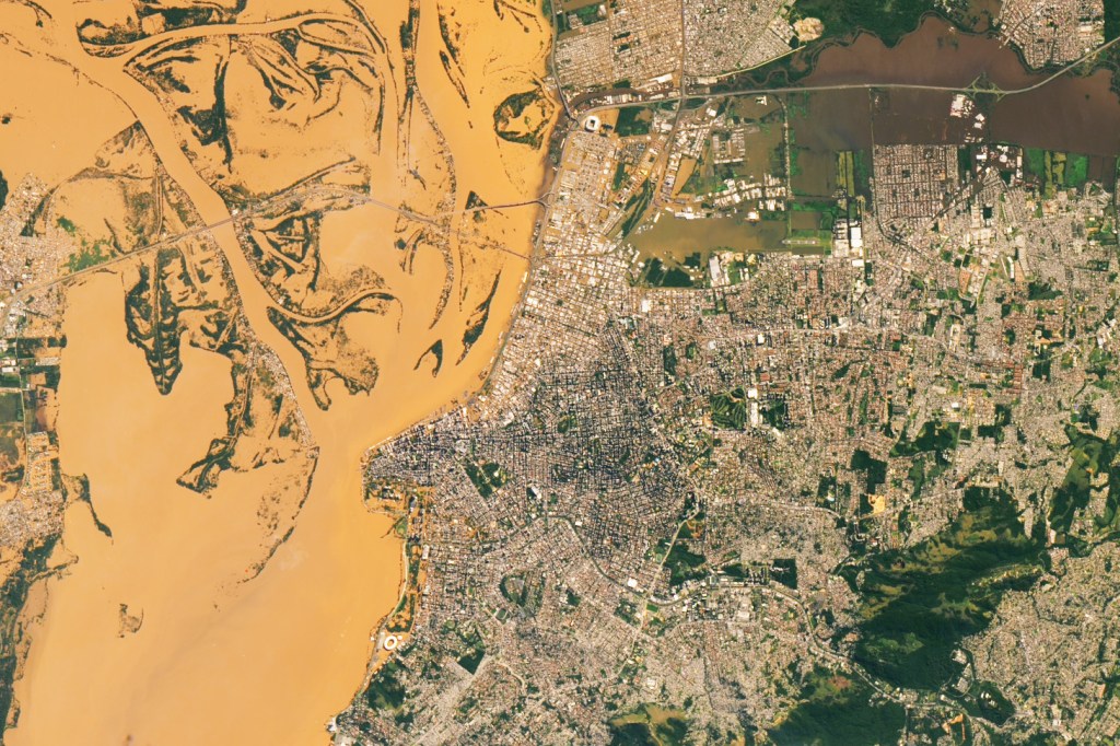 The Jacui River at Rio Grande do Sul shows the already wide river banks being breeched by the rivers mocha brown waters. Within the river banks numerous islands in the river's delta now appear as only river bars. The main city shows roadway between rooftops the same color as the river unlike further inland where roads between homes appear dark from asphalt. The Salgado Filho International Airport field has disappeared entirely beneath the floodwaters.