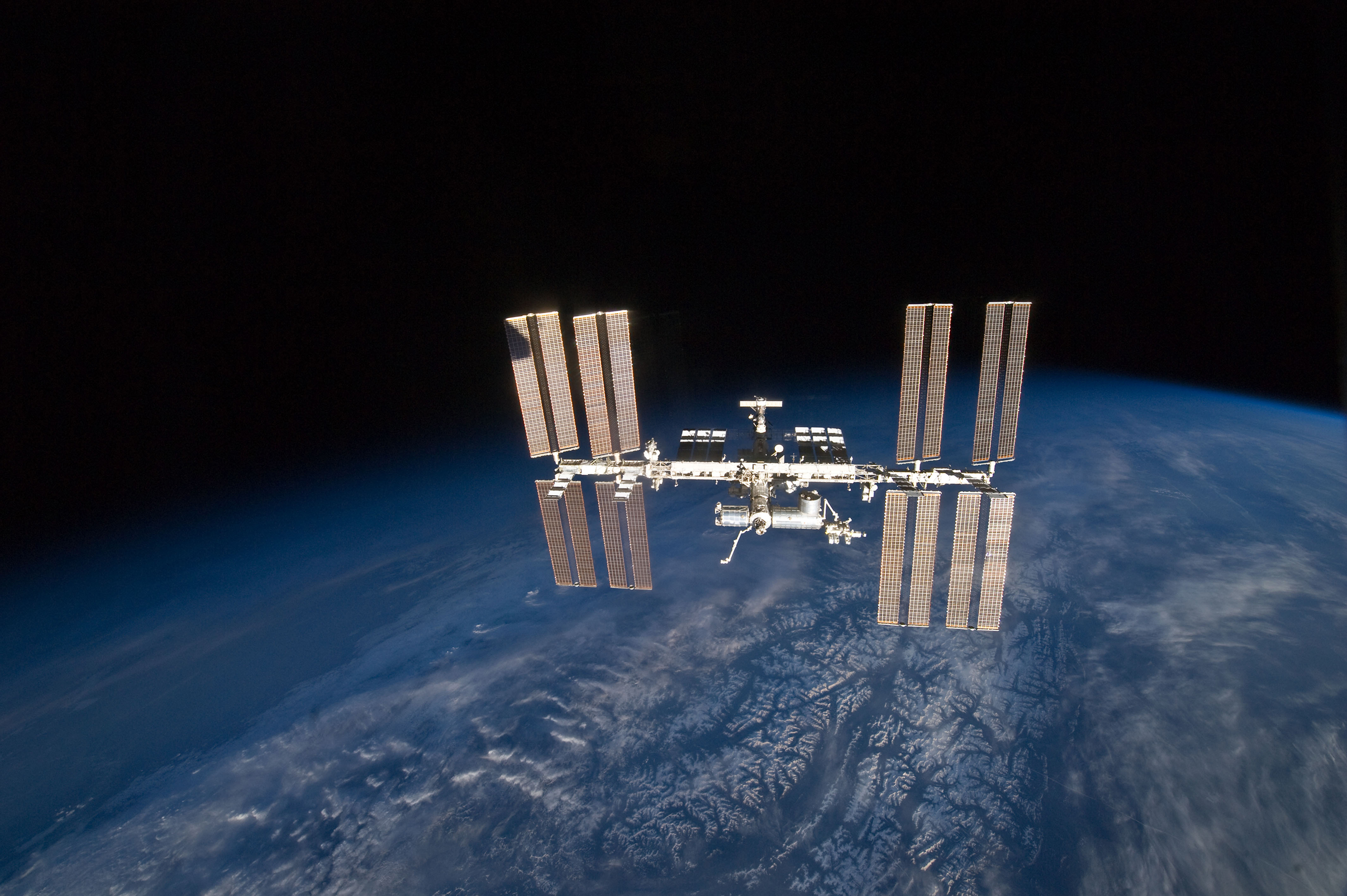 A photo showing view of the International Space Station in its entirety, with the curving blue, clouded surface of Earth below.