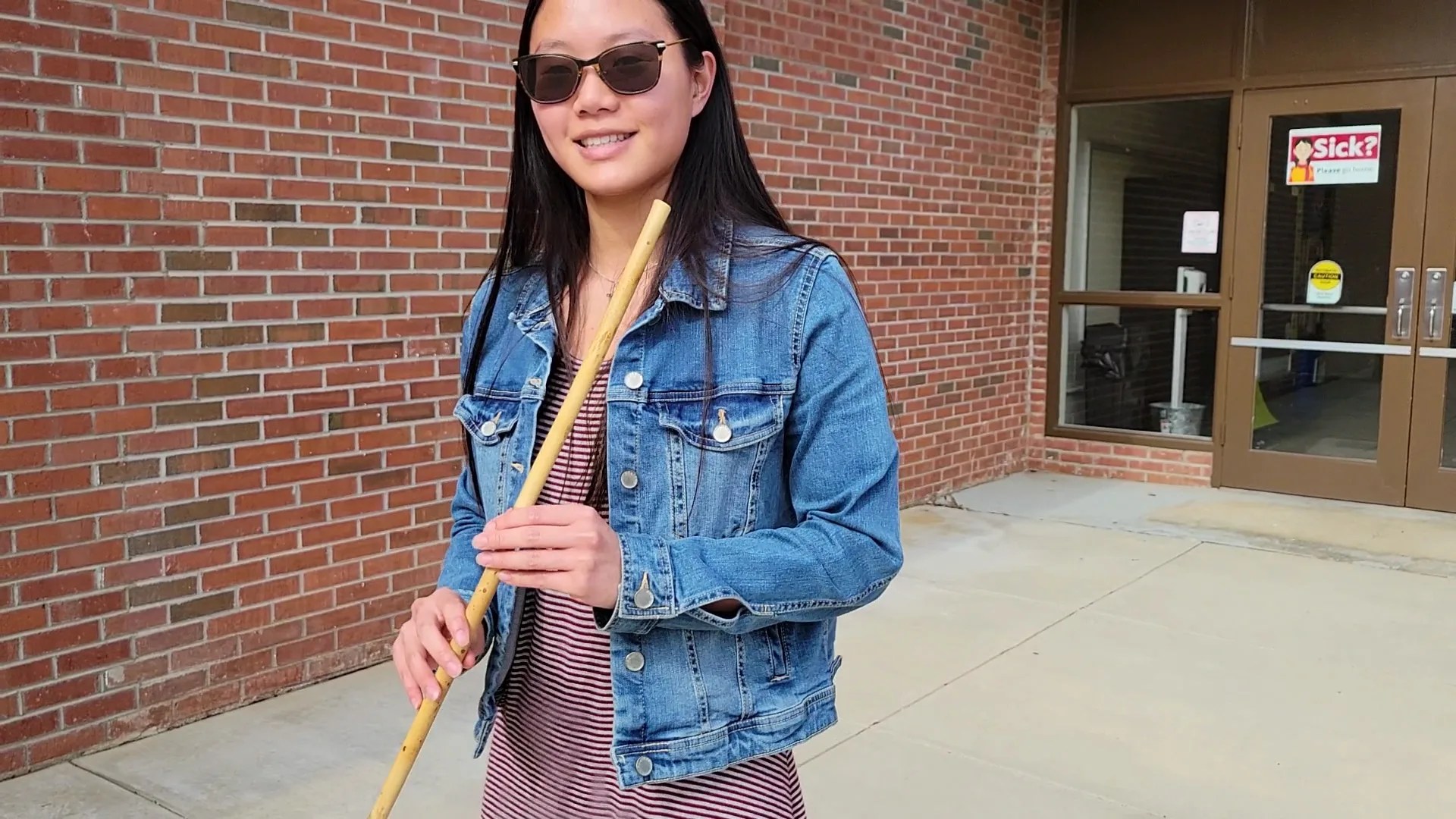 Photo of a woman with long dark hair wearing sunglasses and holding a river cane stick.