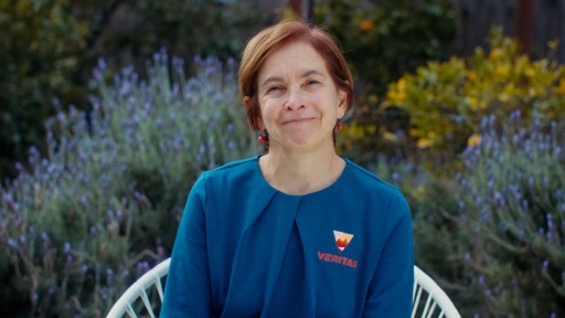 Dr. Sue Smrekar sits for a photo in a garden. She's wearing a blue top with the VERITAS logo.