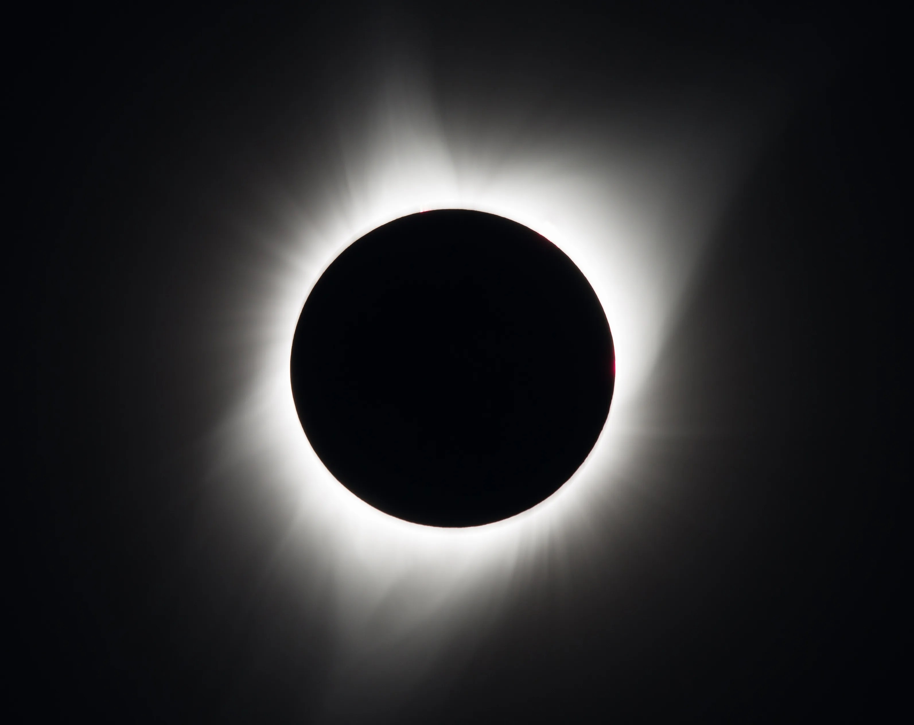 The Sun's wispy, white corona peeks out from behind the dark circular silhouette of the Moon