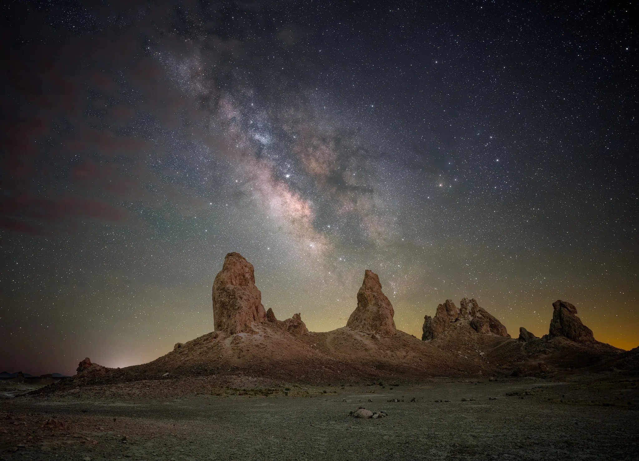 A nighttime photo shows a landscape of pointy, or pinnacle-shaped, rock formations, with the Milky Way as a glowing, diagonal band in the sky.