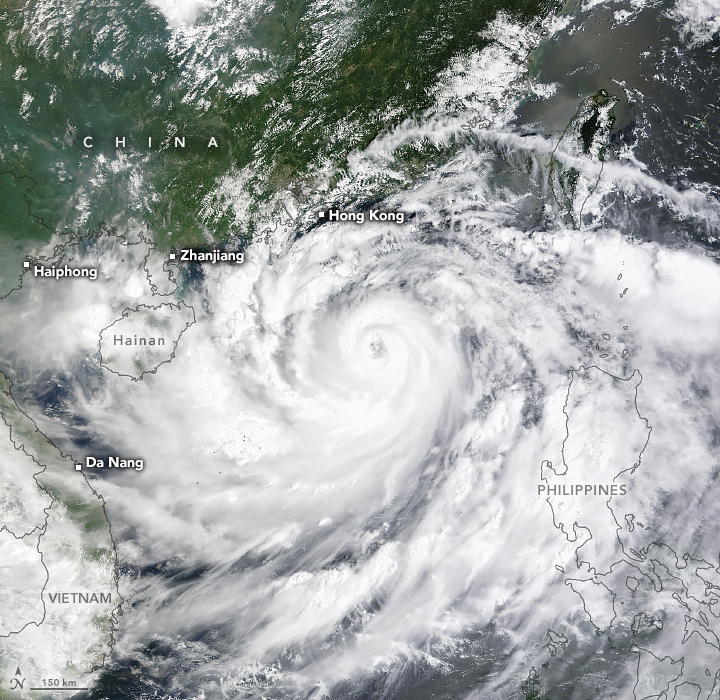 Swirling clouds obscure most of the image. The Philippines are labelled and the coastal outline is superimposed over the clouds. Vietnam and Da Nang are pictured right, slightly visible beneath a layer of clouds. The cloud coverage gives way in the upper third, showing the green landmass of China and with Hong Kong on the very edge of the densest cloud cover. Cities of Zhanjiang and Haiphong are also labelled as coastal cities further to the left of the storm center. The Island of Hainan is outline is super imposed on the clouds in the center left of the image.