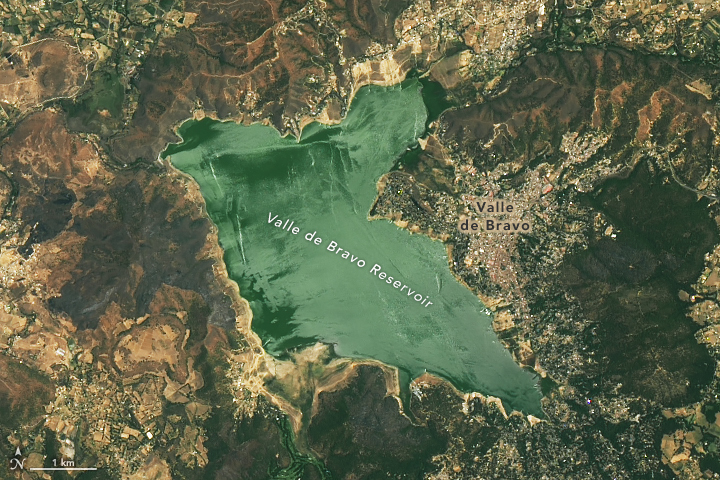 The blue-green water of the reservoir, centered in this image, has shrunk as formerly submerged lakebed appears around the reservoir. It is particularly noticable in the upper right and lower left of the image, where a population center stretches piers to the water an inordinately long distance from the road and population center.