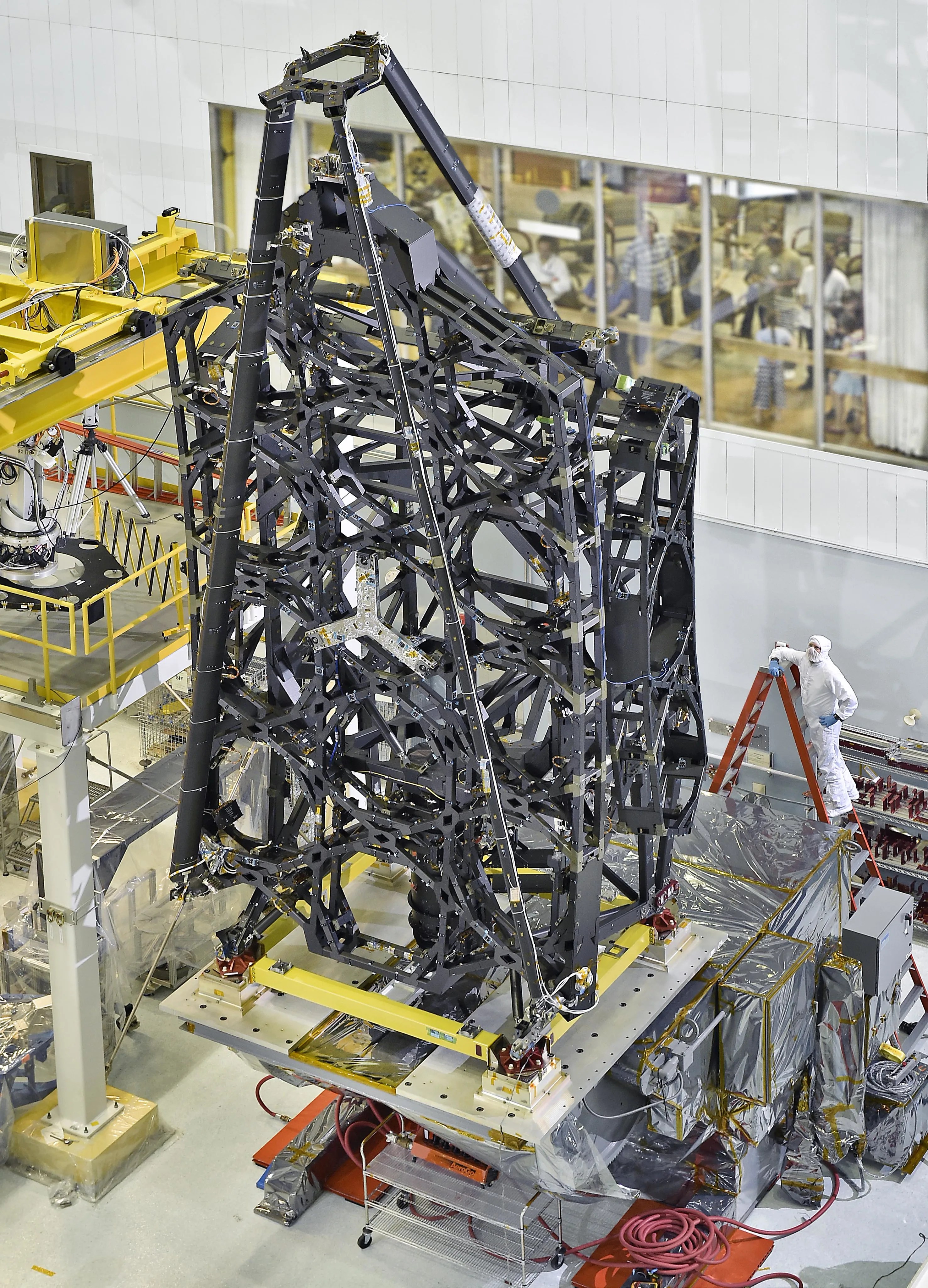 An engineer stands on a ladder next to NASA's James Webb Space Telescope Structure.