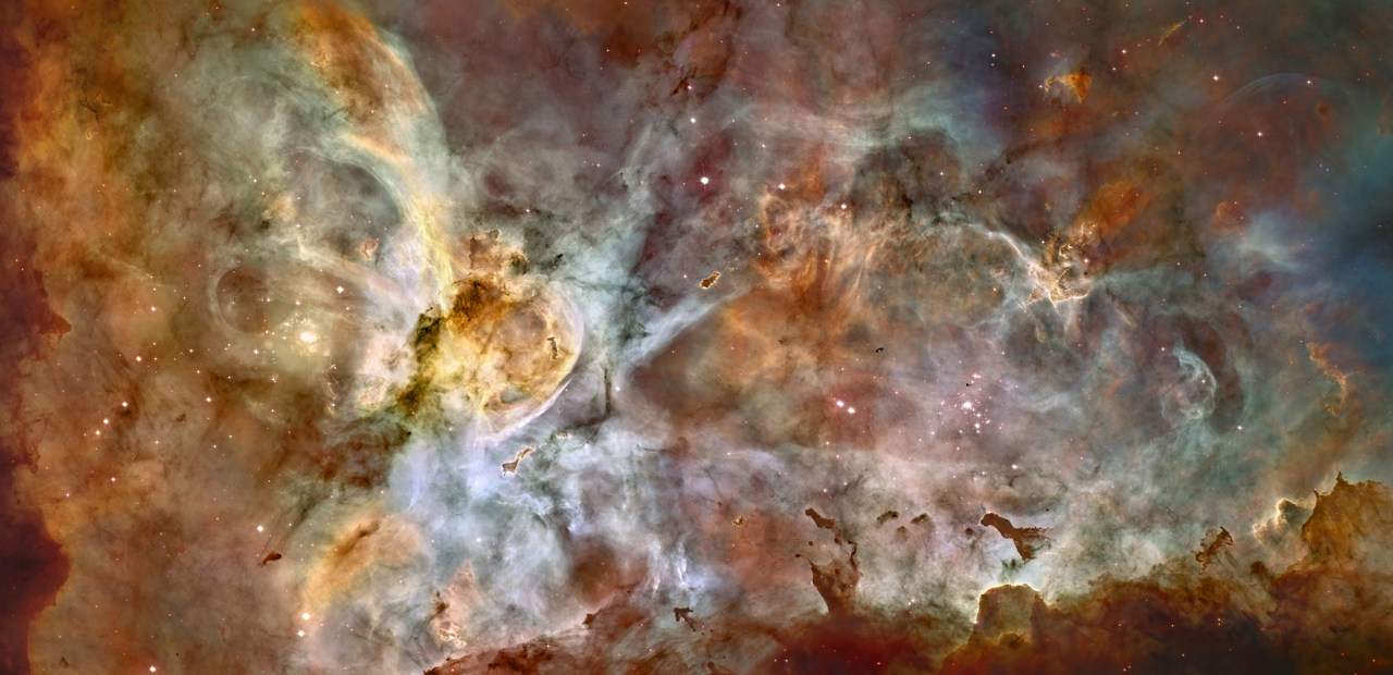 Entire image is filled with green, brown, rusty colors of the Carina Nebula. Chaotic groupings of this dust and gas with stars dispersed randomly throughout the image.