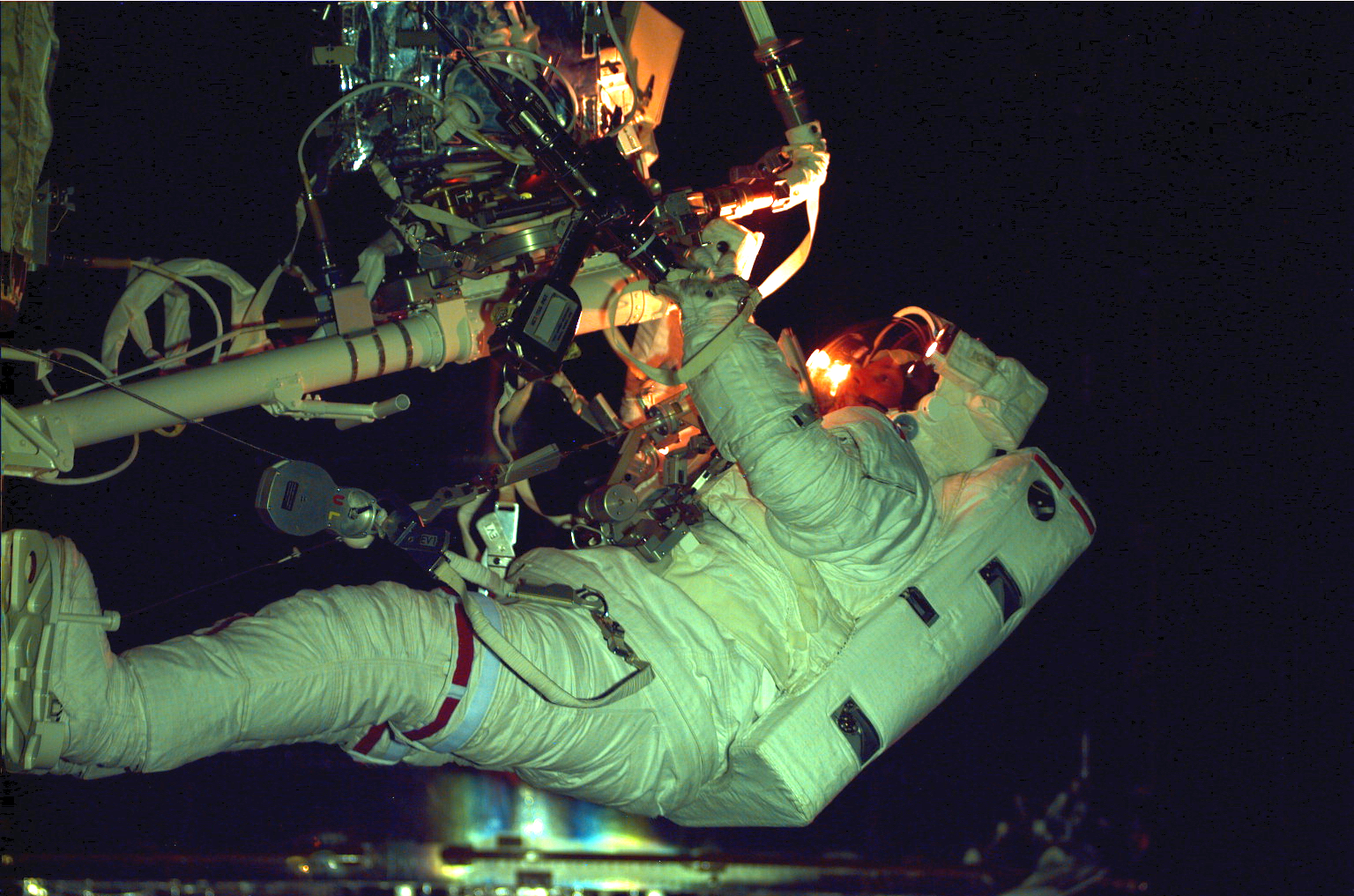 An astronaut with many tools attached to a workstation in front of him.