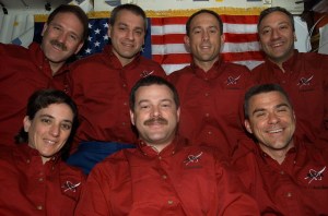 The STS-109 crew poses for a photo in front of an American flag in the crew cabin of the shuttle.