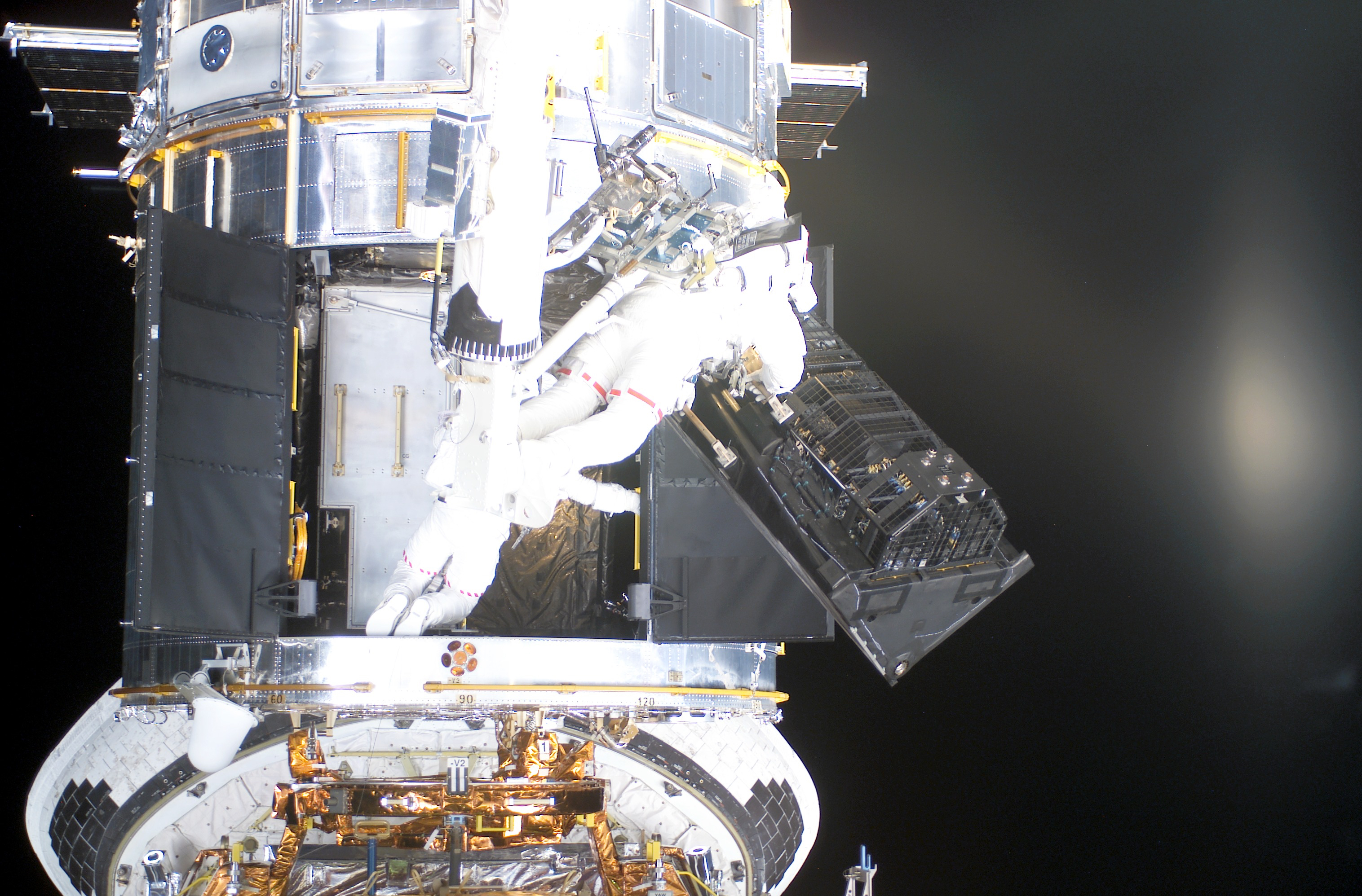 Two astronauts removing an instrument from the bottom of Hubble.
