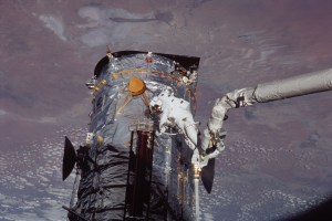 An astronaut at the end of the shuttle's robotic arm works with a solar array.