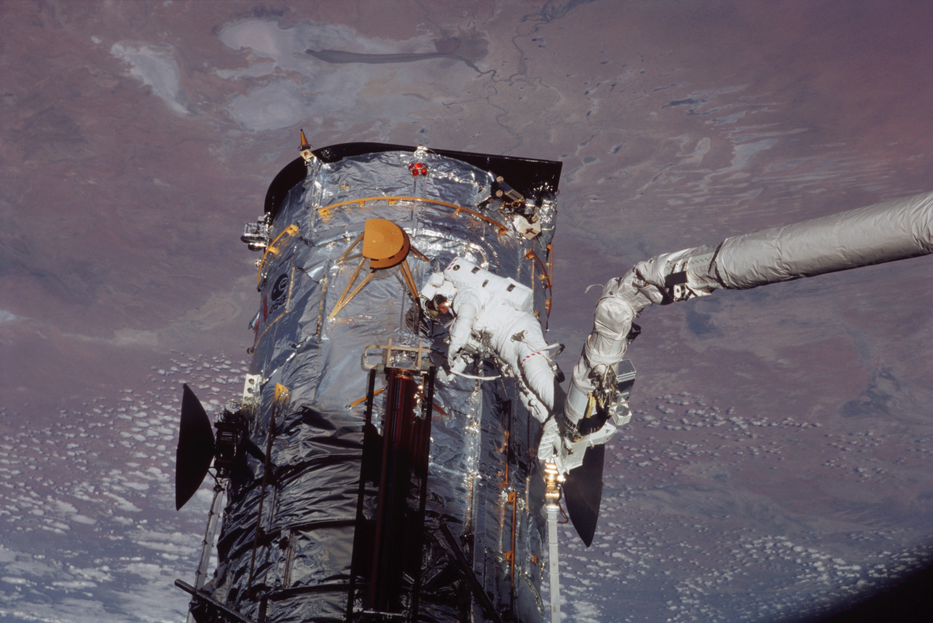 An astronaut at the end of the shuttle's robotic arm works with a solar array.