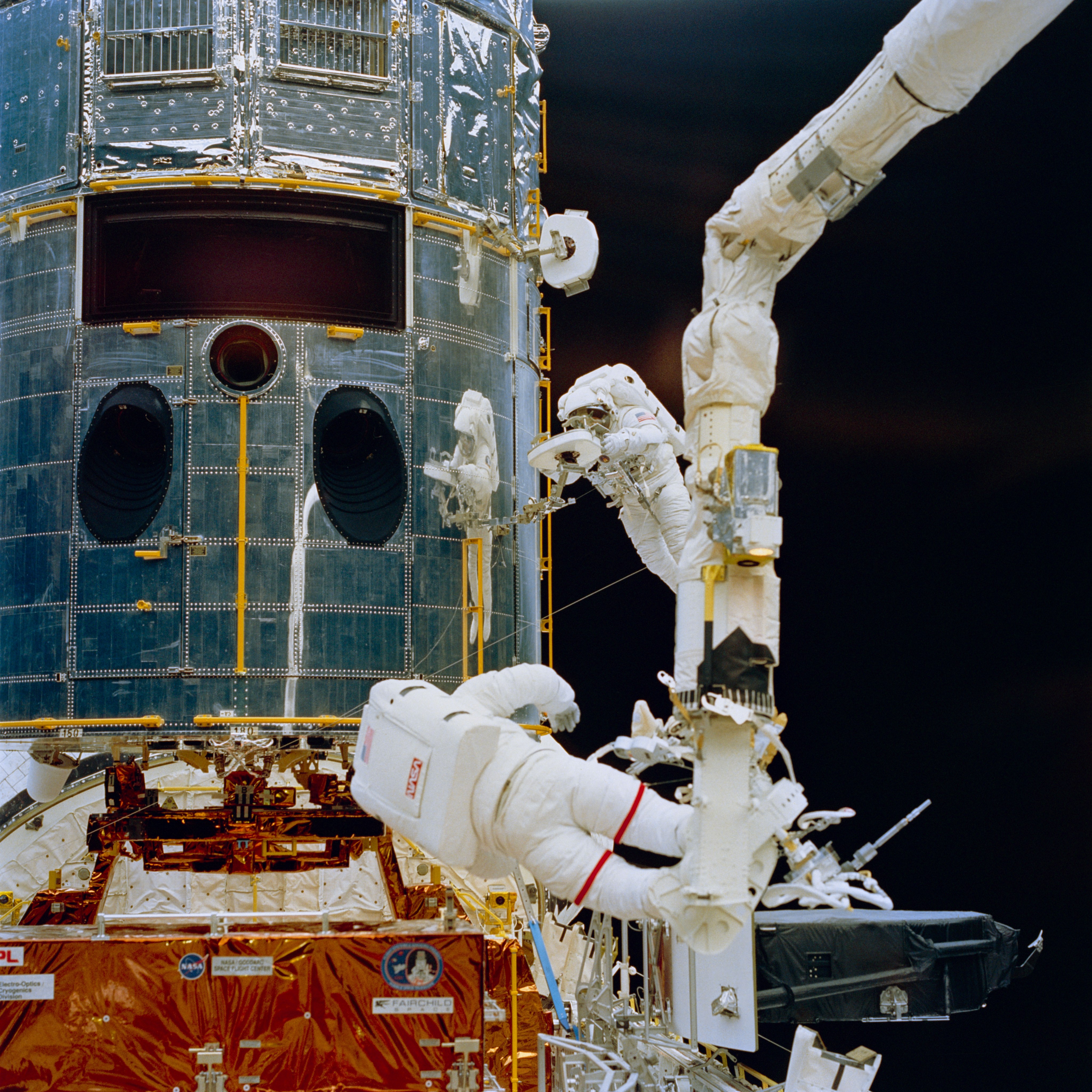 An astronaut on the robotic arm and an astronaut tethered to Hubble service the telescope.
