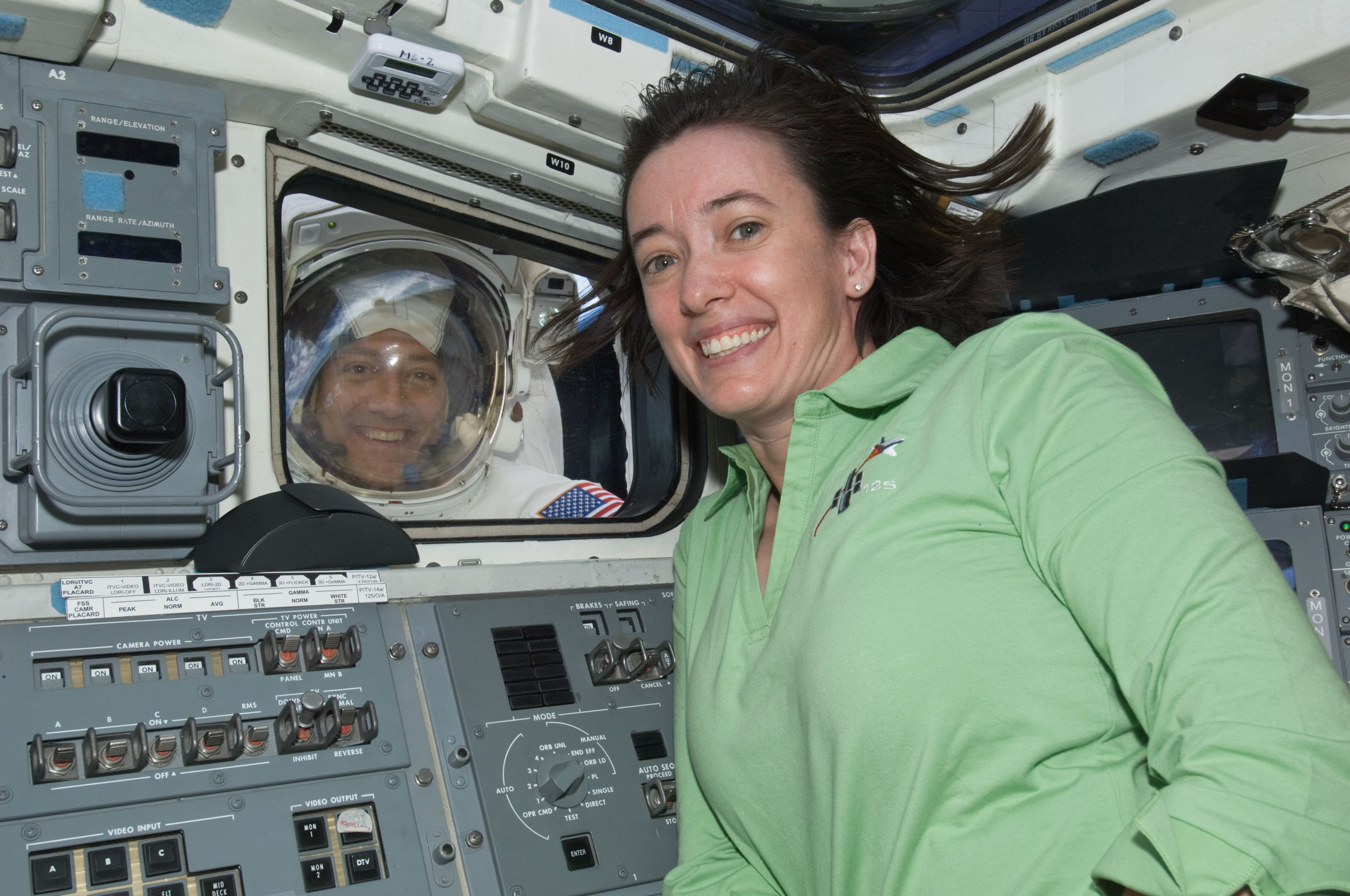 Two astronauts pose for a picture, one inside the crew cabin and one outside.