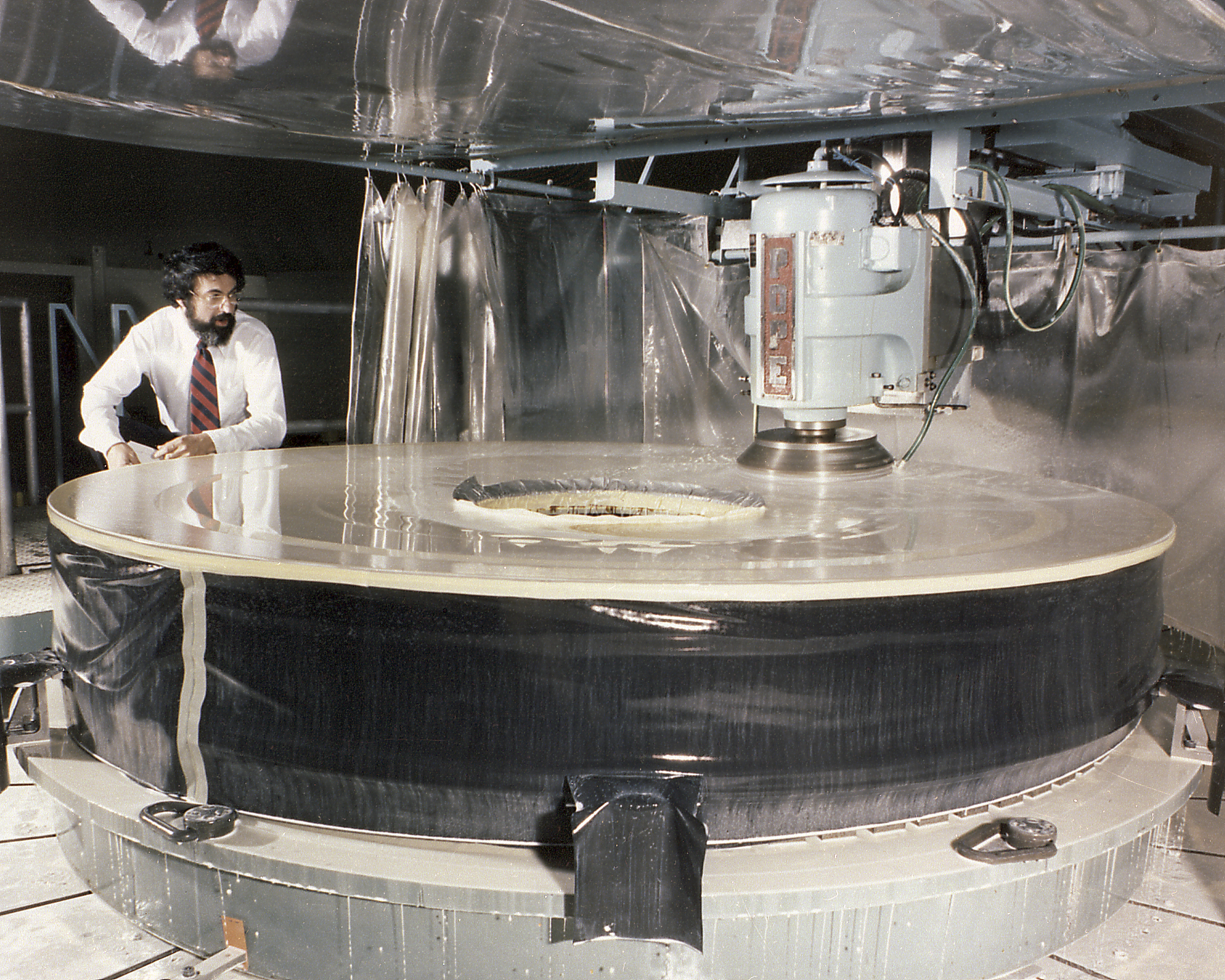 A machine is grinding the primary mirror of Hubble while a person looks on.