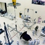 The Wide Field Planetray Camera is being lowered on a crane for installation in a clean room surrounded by engineers.