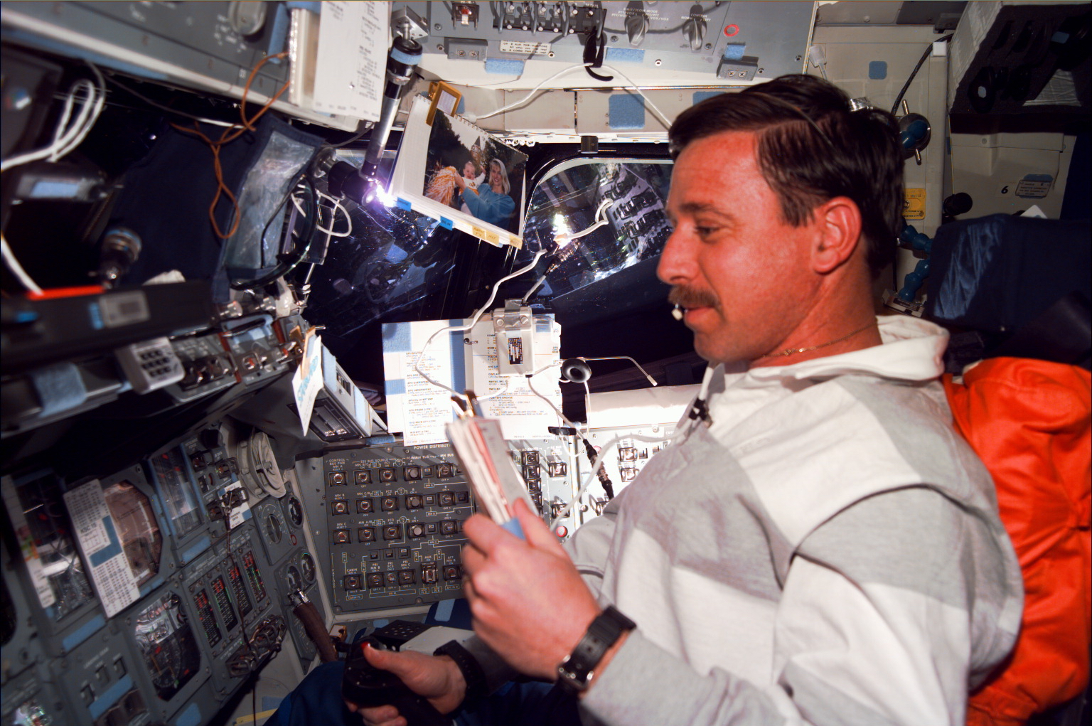 An astronaut on the flight deck of the space shuttle sitting in the pilot's chair.