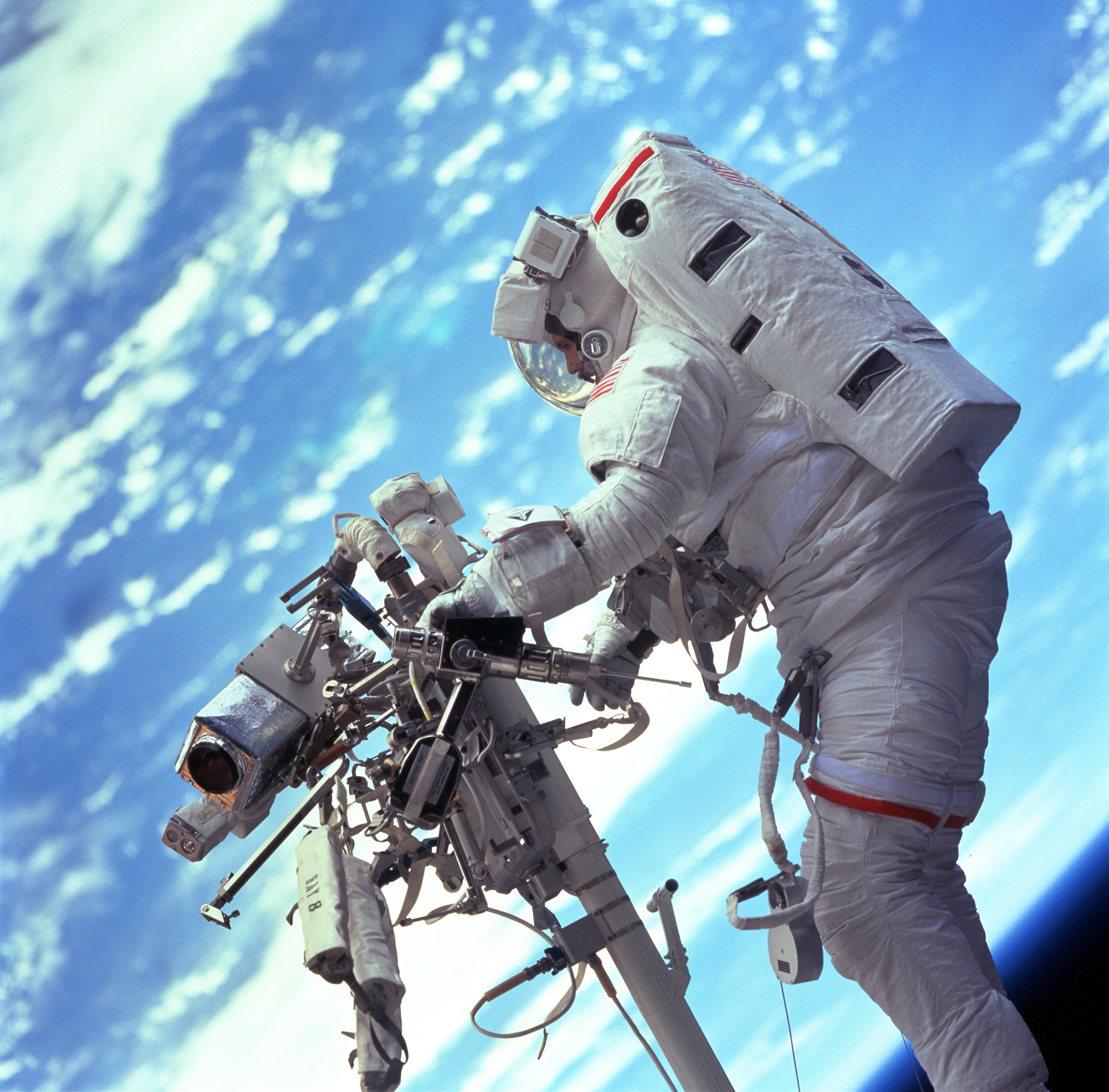 An astronaut on the end of the robotic arm with numerous tools. The blue earth is in the background