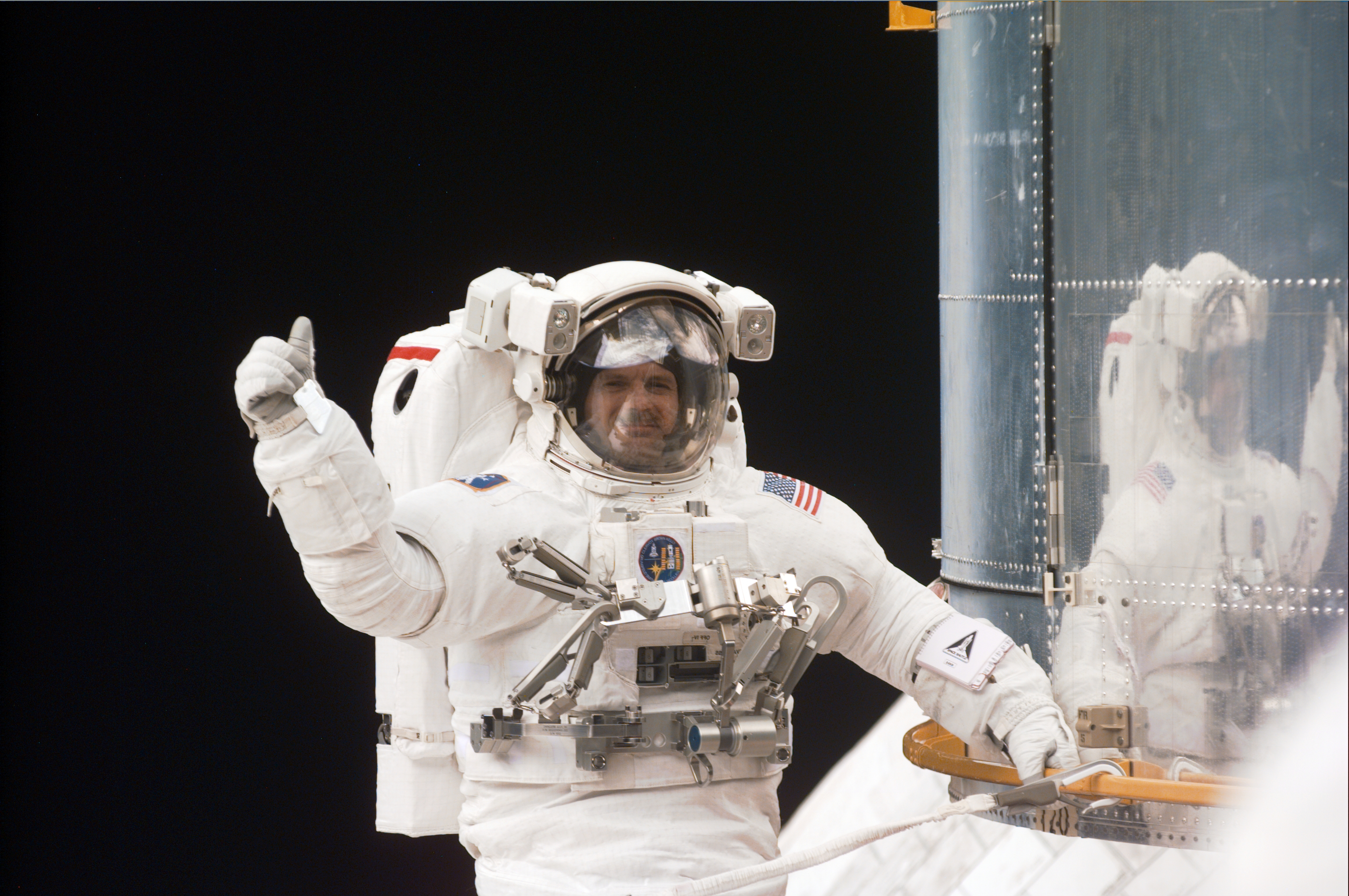 An astronaut gives the thumbs up. while attached to the bottom of Hubble.