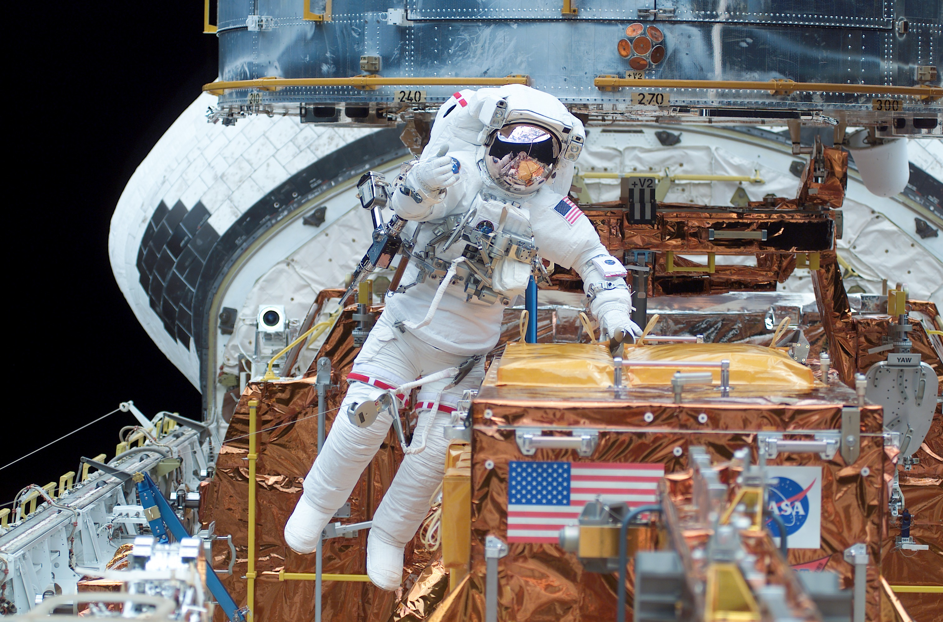 An astronaut floats in the cargo bay next to a gold carrier.