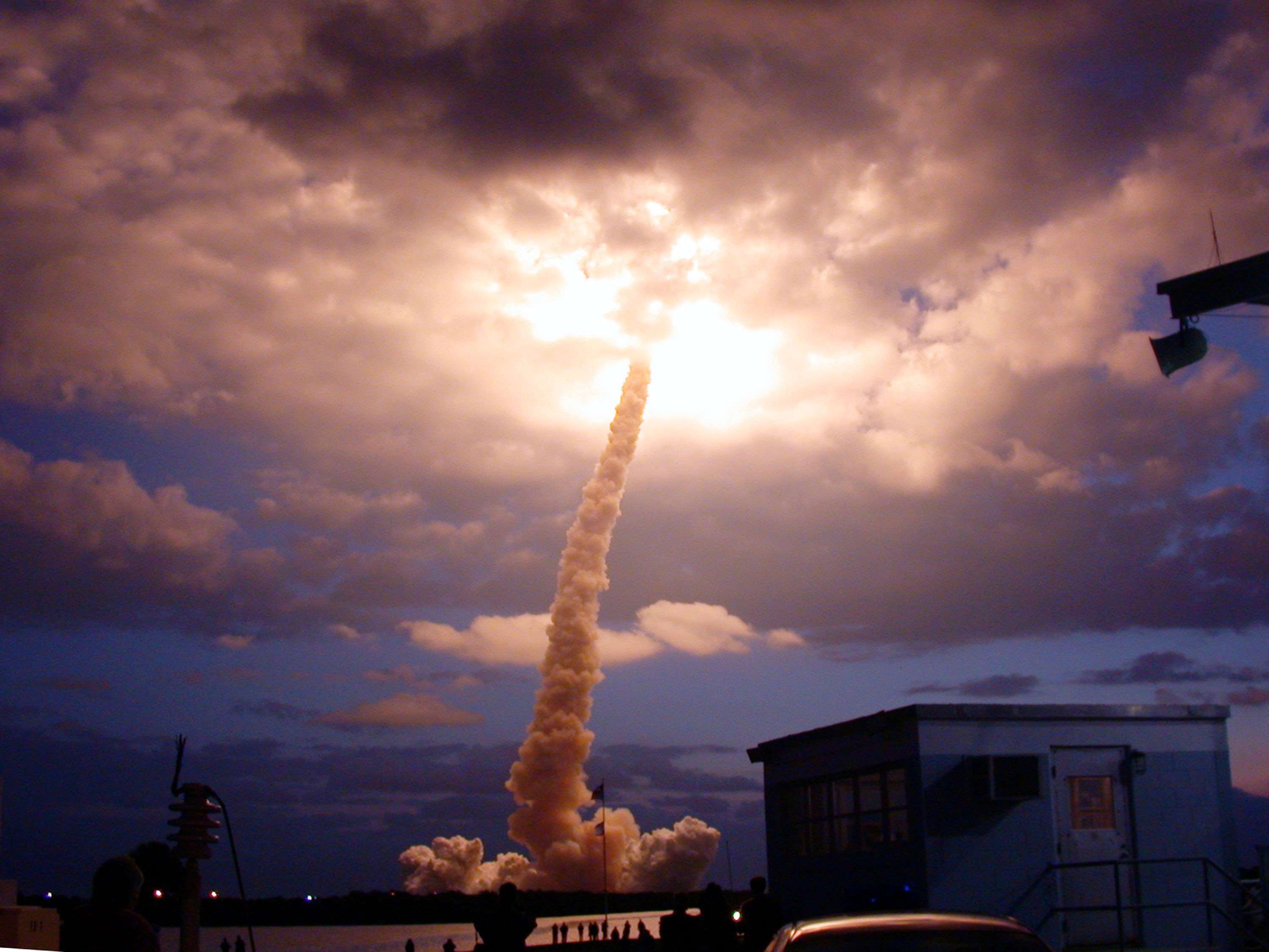The space Shuttle launches into a cloud,illuminating the cloud from the inside out, with a trail of smoke behind it.