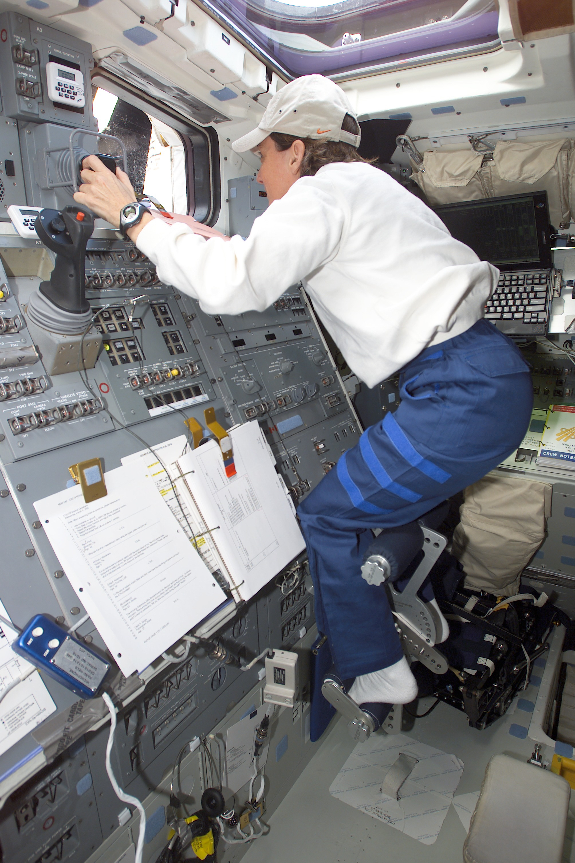 An astronaut floats on the flight deck, her feet anchored, as she works the controls for the robotic arm.