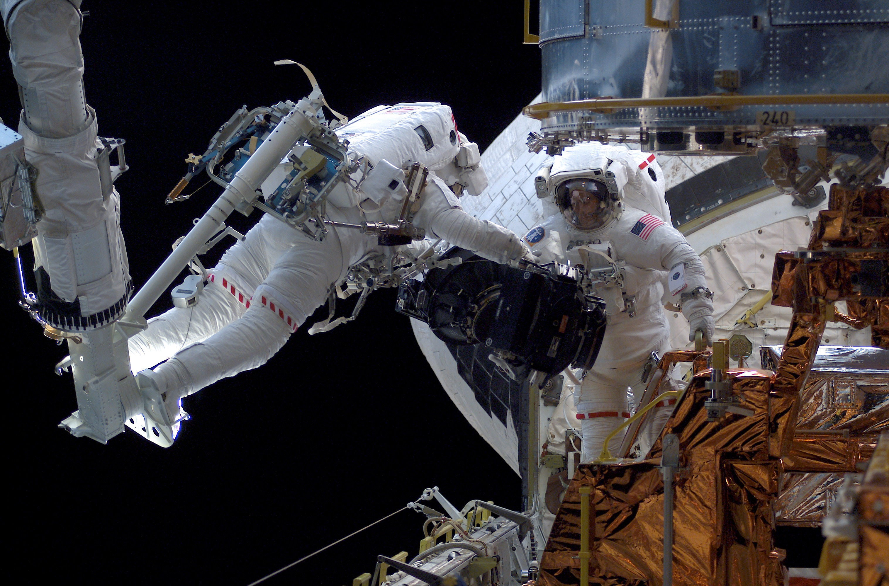 One astronauts hand some telescope hardware to another in the cargo bay.