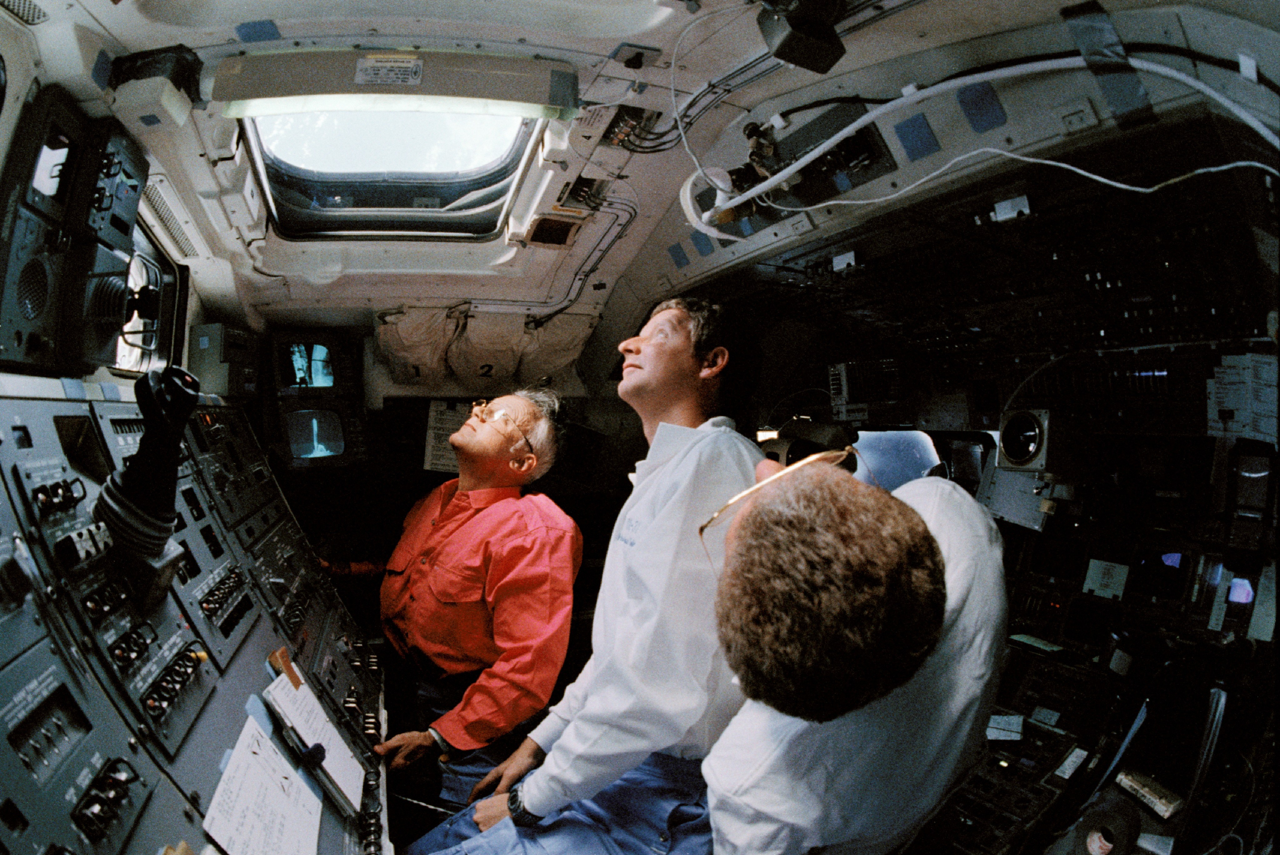 Three astronauts look through the roof windows and monitor Hubble.