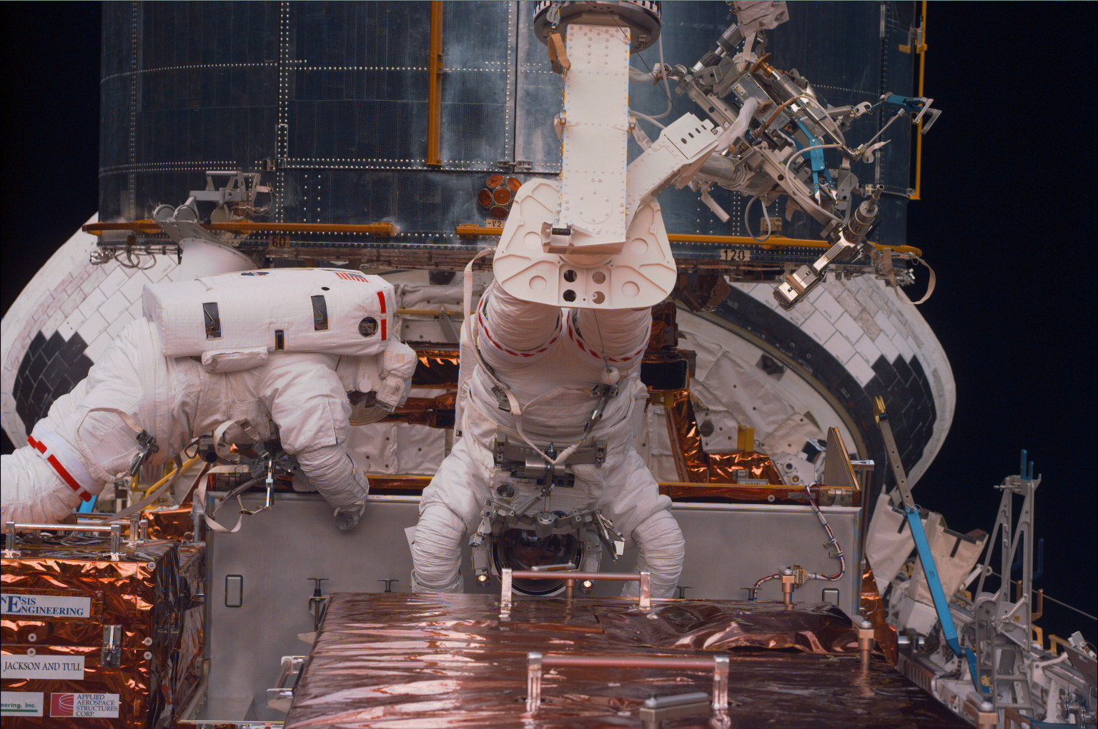 Two astronauts work on removing a fine guidance sensor from a carrier in the Shuttle's cargo bay.