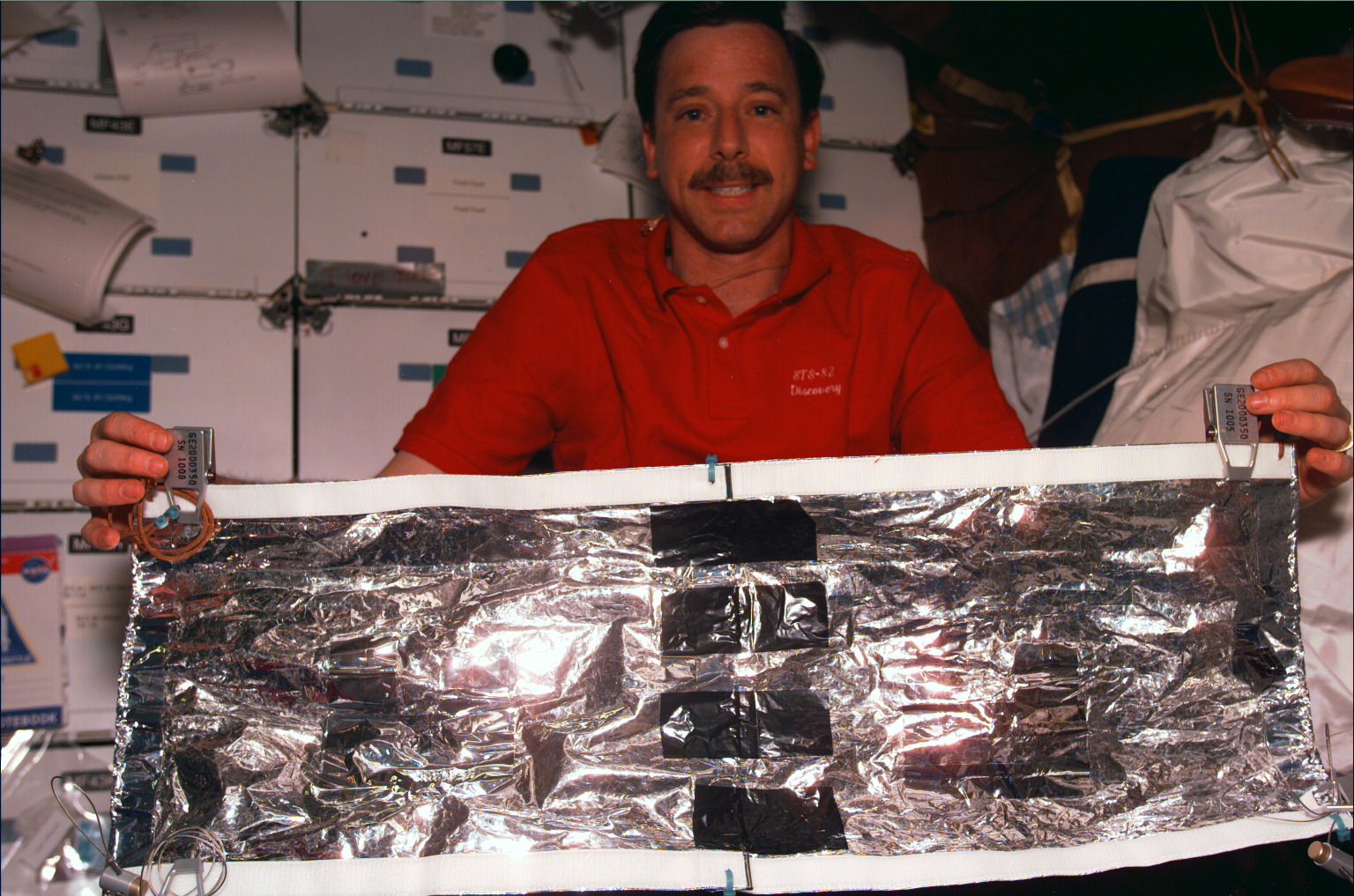 An astronaut inside the cabin holds an insulating spacecraft blanket that they made.