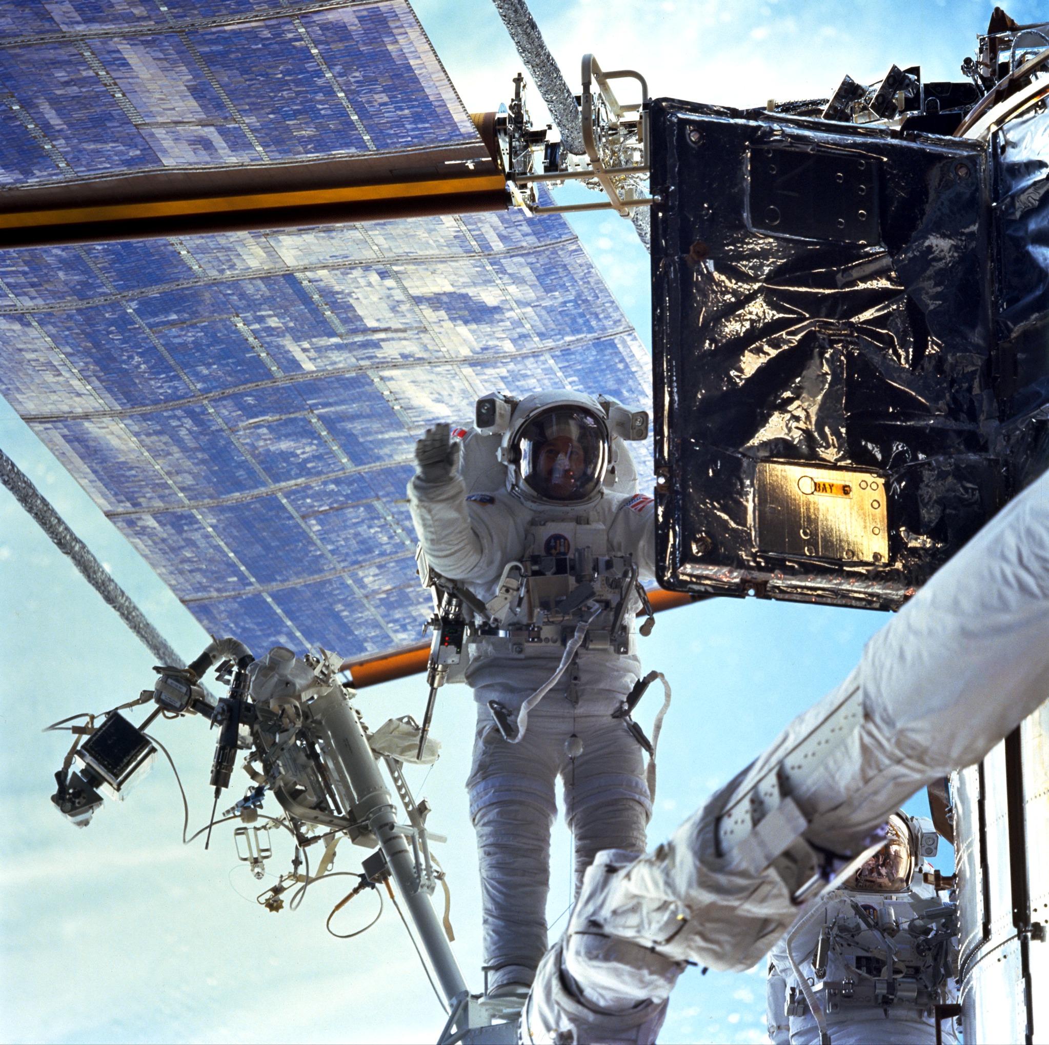 An astronaut on the end of the robotic arm opens an equipment door on Hubble. The solar array and the blue earth are in the background.