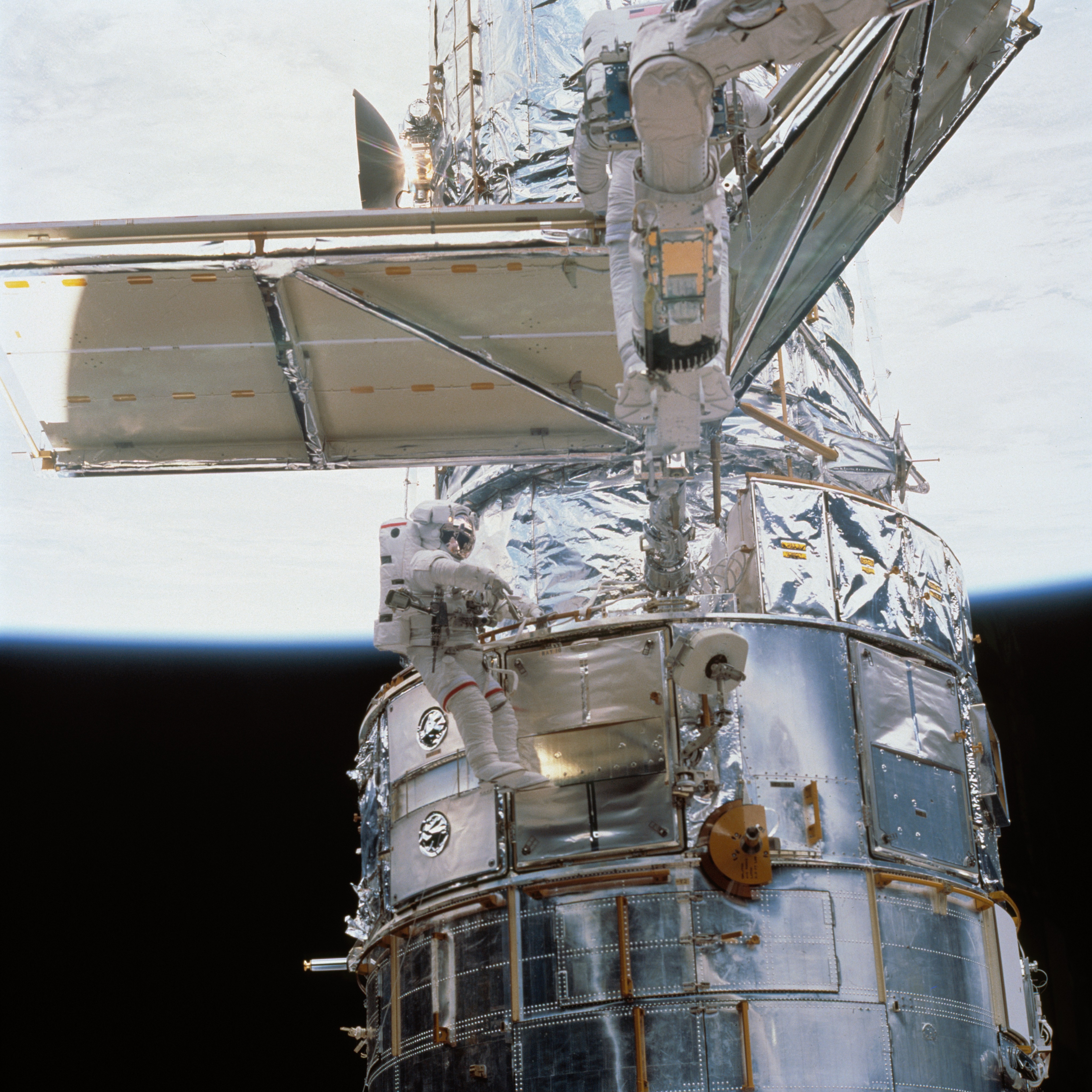 Two astronauts install a new solar panel on Hubble, one of them is unfolding it.