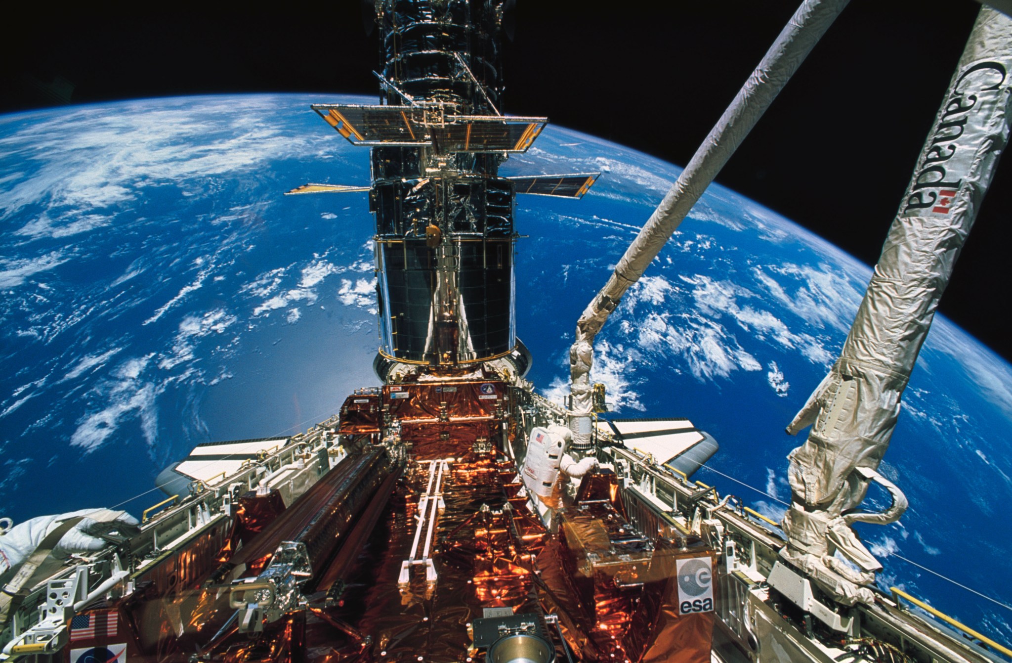 An astronaut working in the cargo bay a very blue earth in the background.