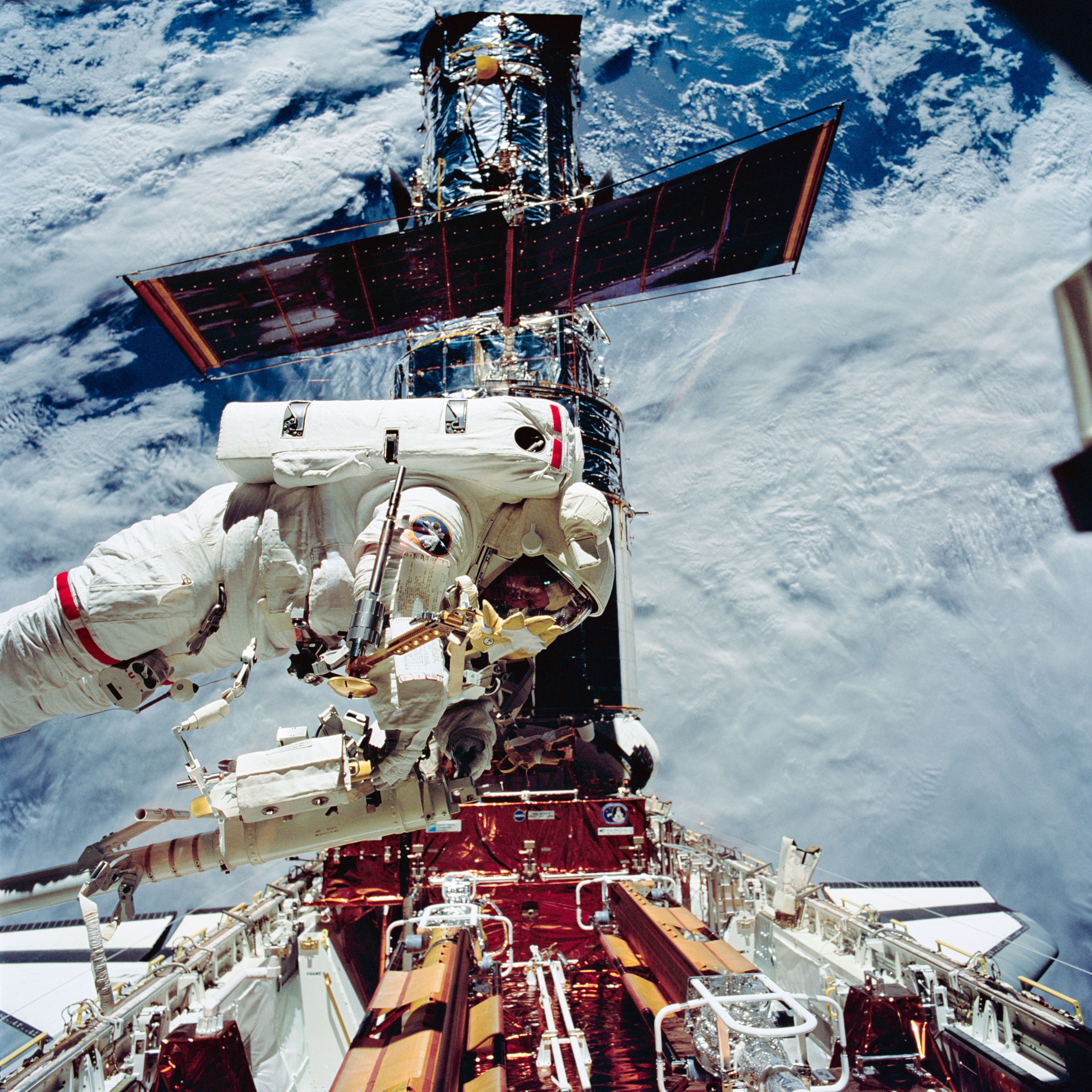 An astronaut on the end of the robotic arm with Hubble and the Earth behind her.