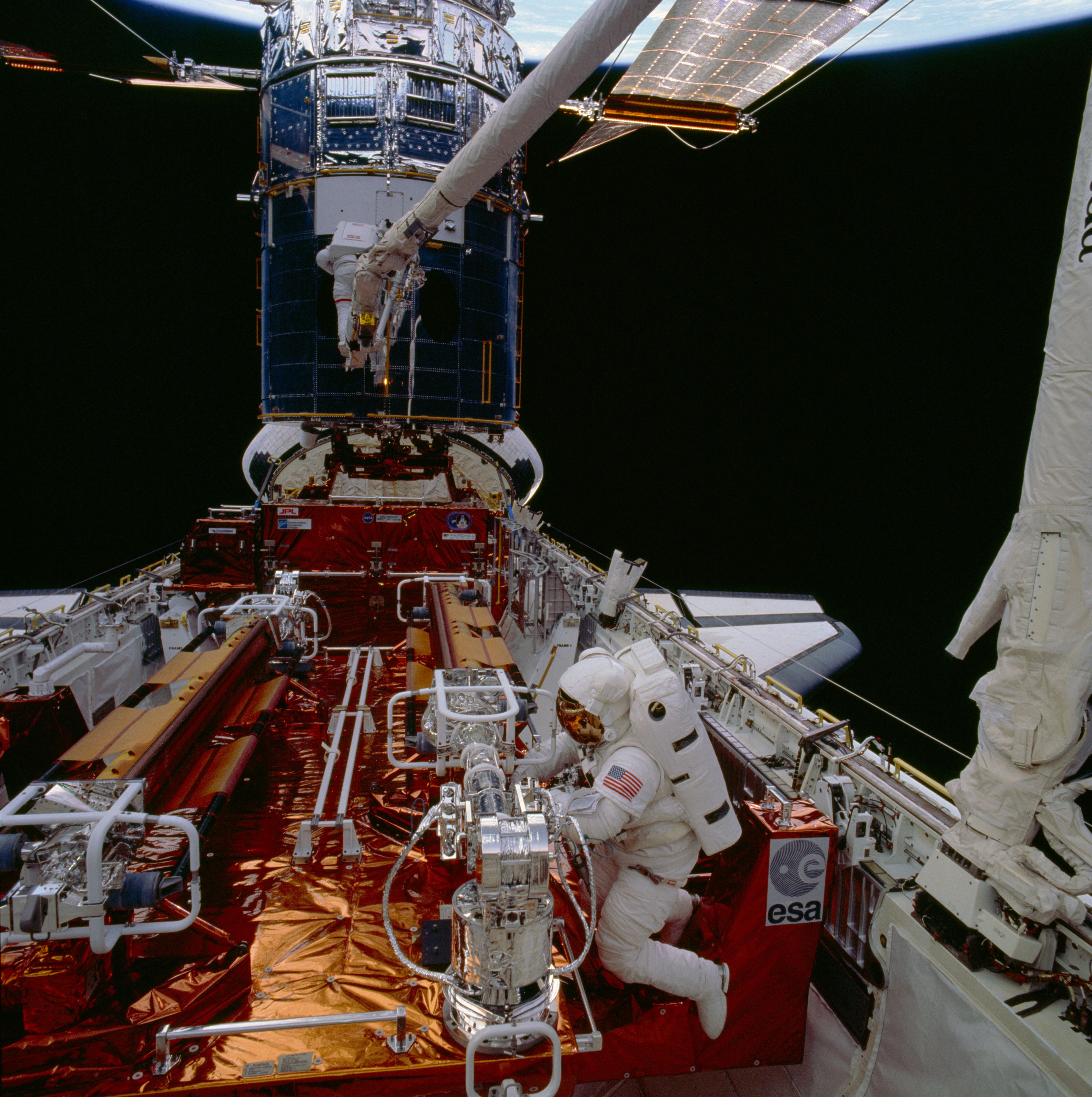 An astronaut on the robotic arm and one in the cargo bay of a Hubble mission
