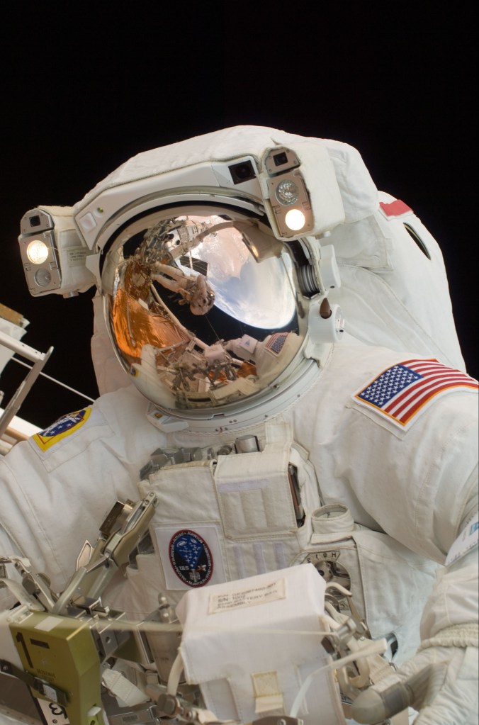 An astronaut getting his photo taken with the earth and the astronaut with the camera in the reflection of his visor.