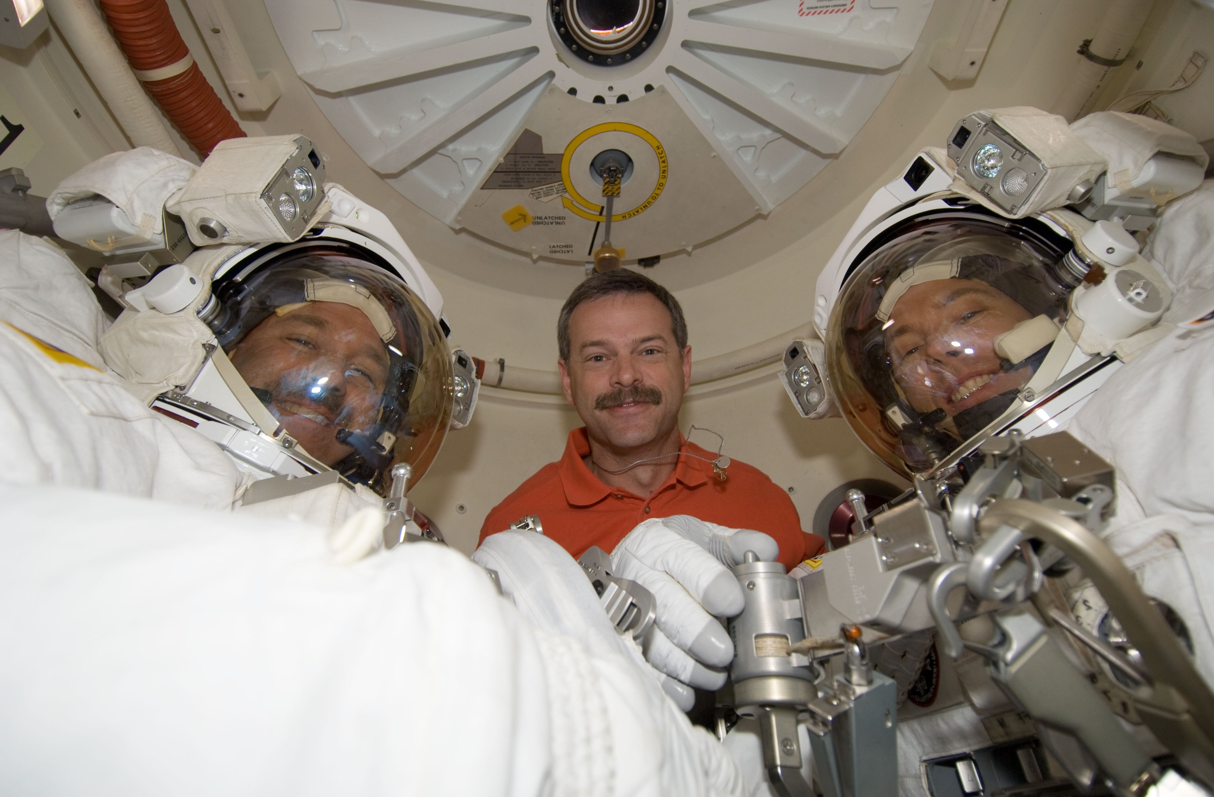 Three people in the airlock, the commander and two astronauts suited up for a spacewalk, pose for a picture.