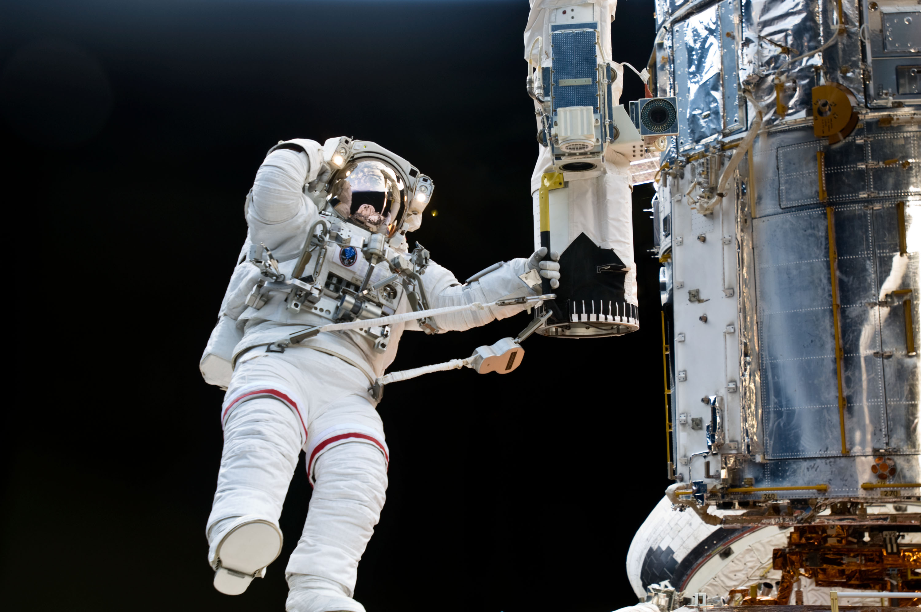 An astronaut tethered to the end of the Shuttle's robotic arm to the left of Hubble.