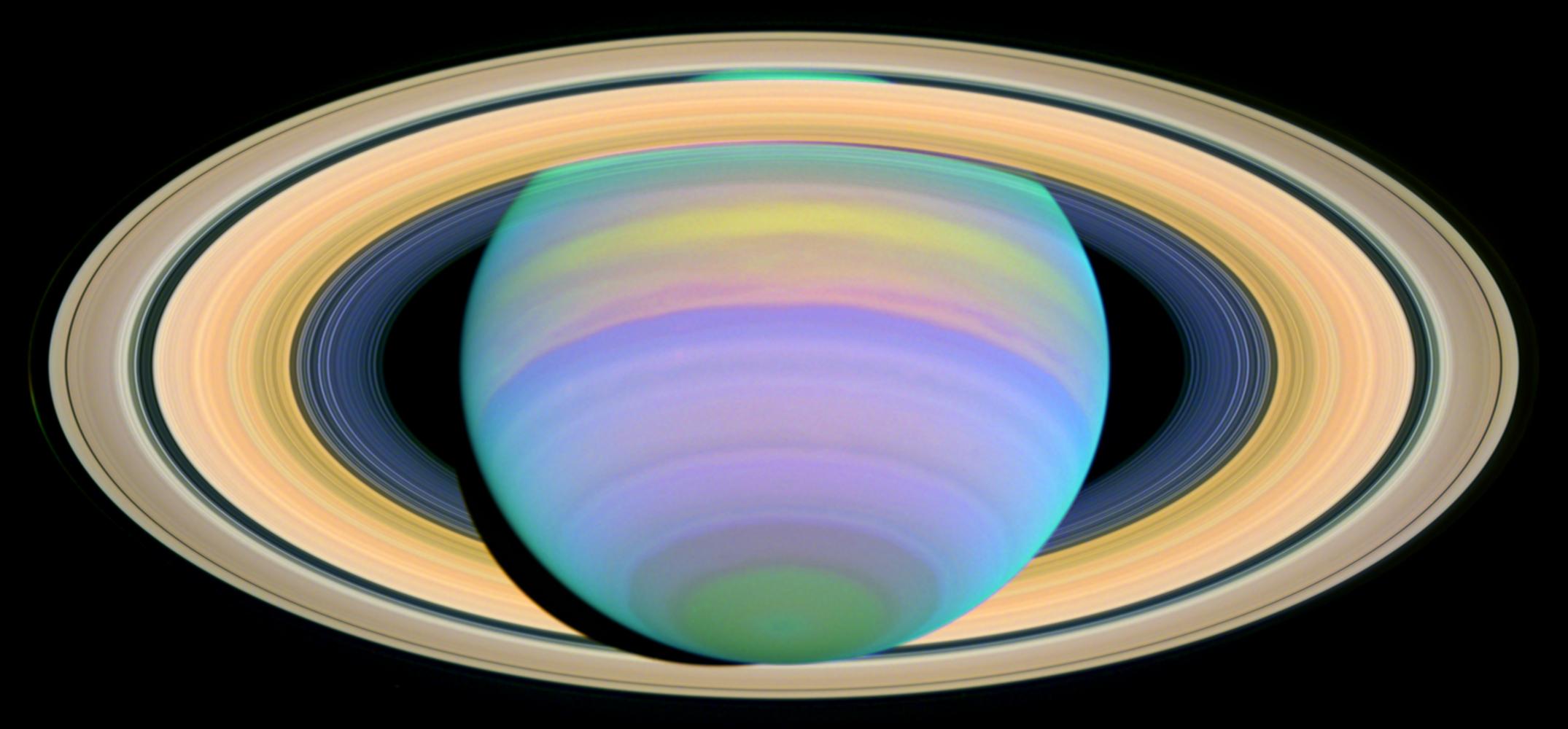 Saturn, seen in purples, greens and blues, is surrounded by its bright yellow rings.