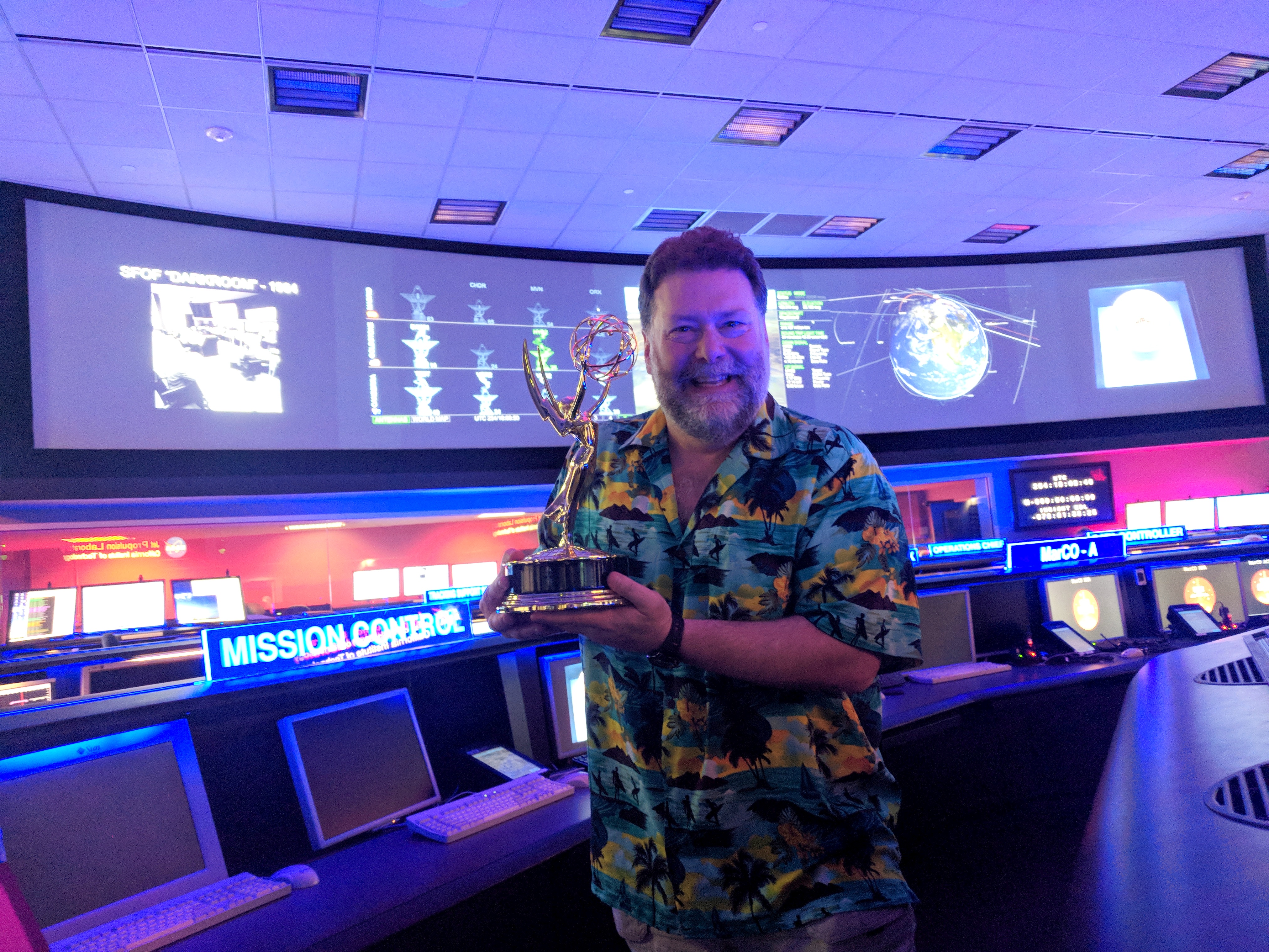Todd in mission control holding an Emmy award statue.