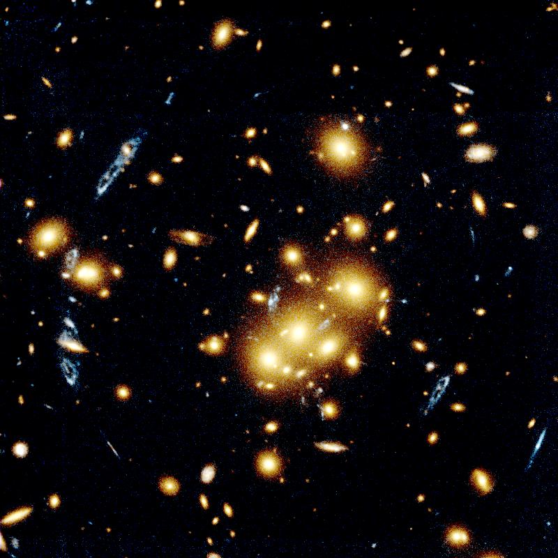 Spots of light that are galaxies in this image. Some of the galaxies appear to be stretched due to gravitational lensing. Three very bright orange spots of light near the center in a row.