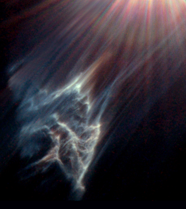 Wisps of dark green dust at the bottom left of the image as a bright star is shining its light from the top right of the image.