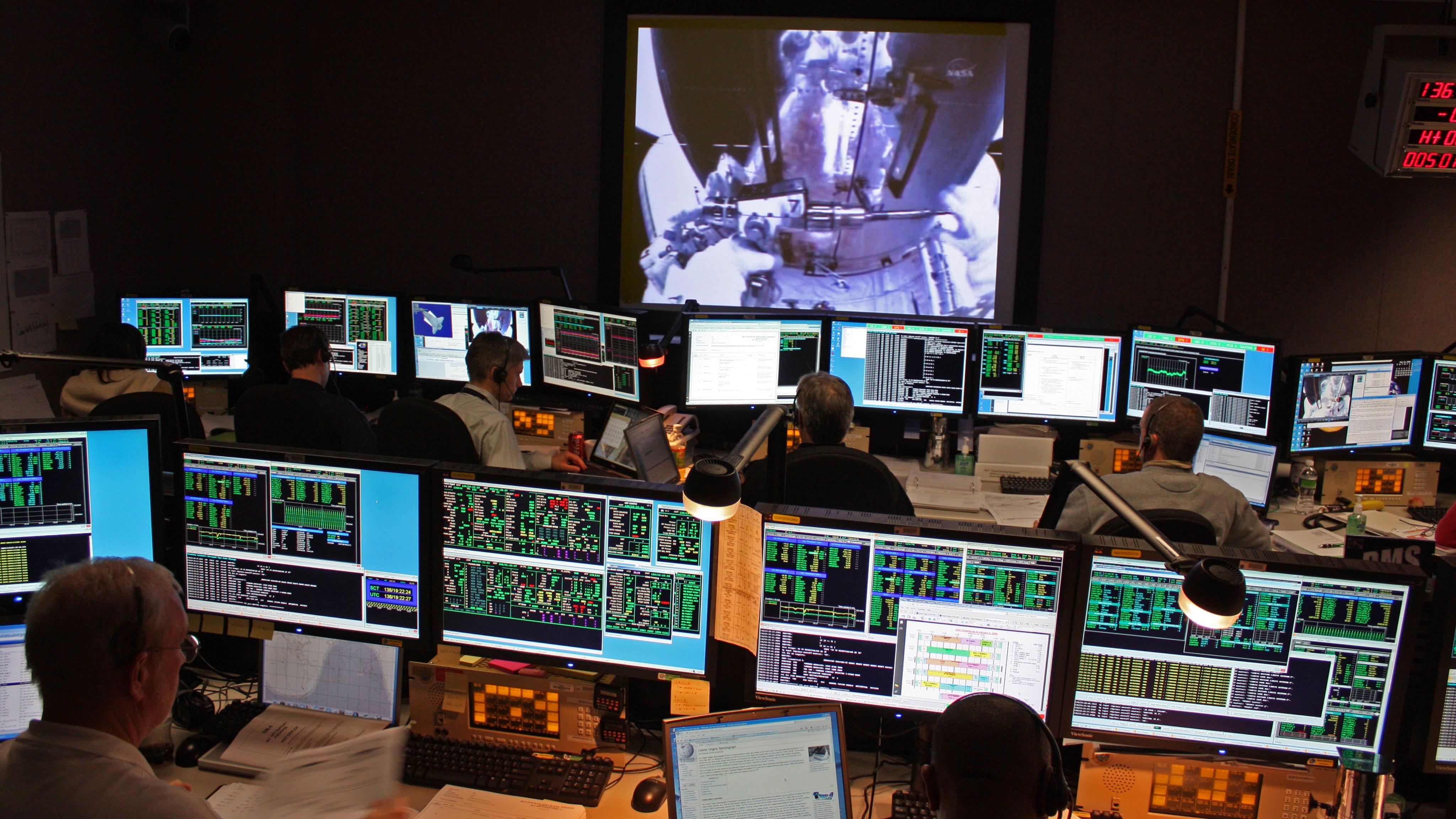 Hubble engineers in the control center watch on large screens the astronauts close the spacecraft's lower doors.