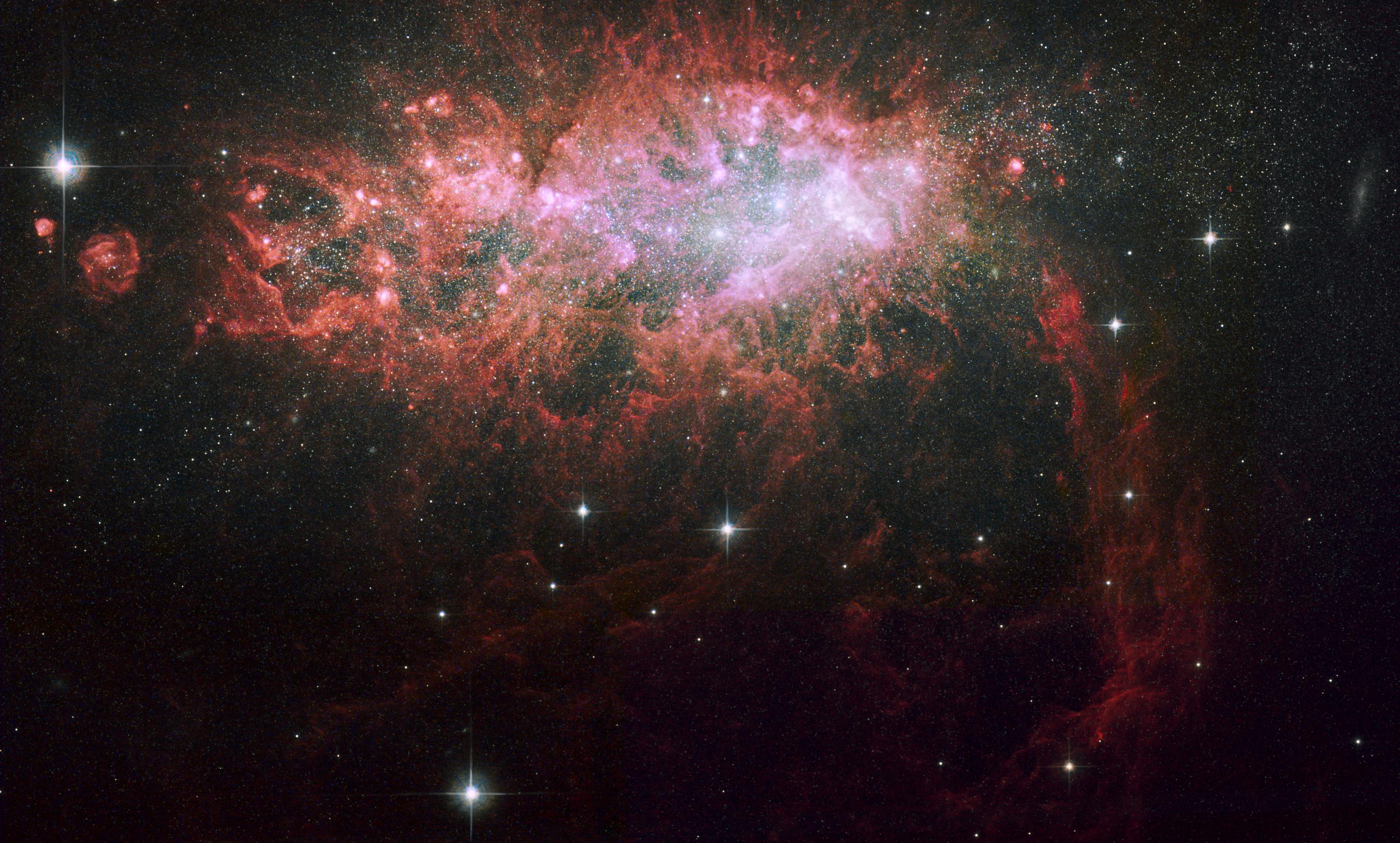 A bright red galaxy shines near the top of the image in shades of pink and white.