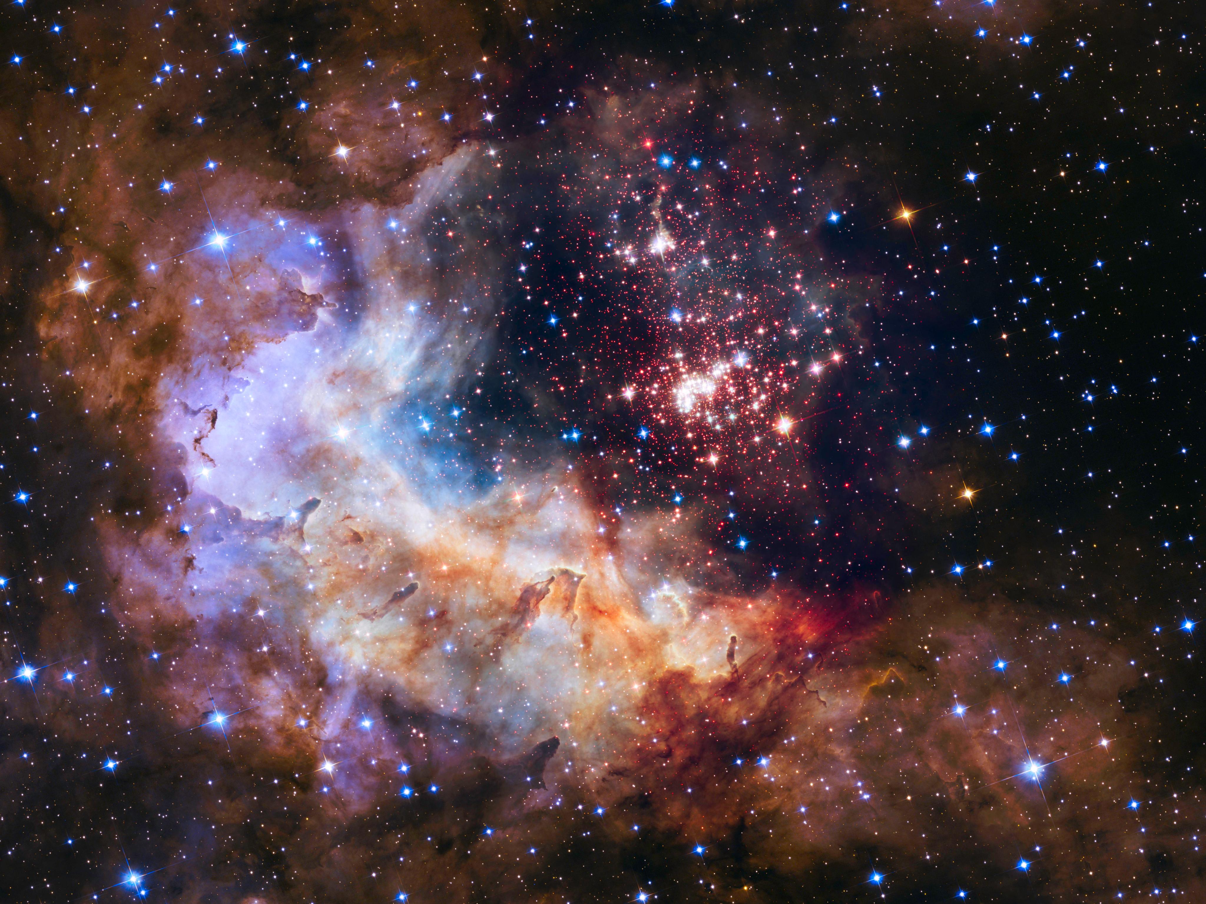 A combintation of yellow, brown, red, and blue/violet colored gas intermixed with blue and yellow stars.