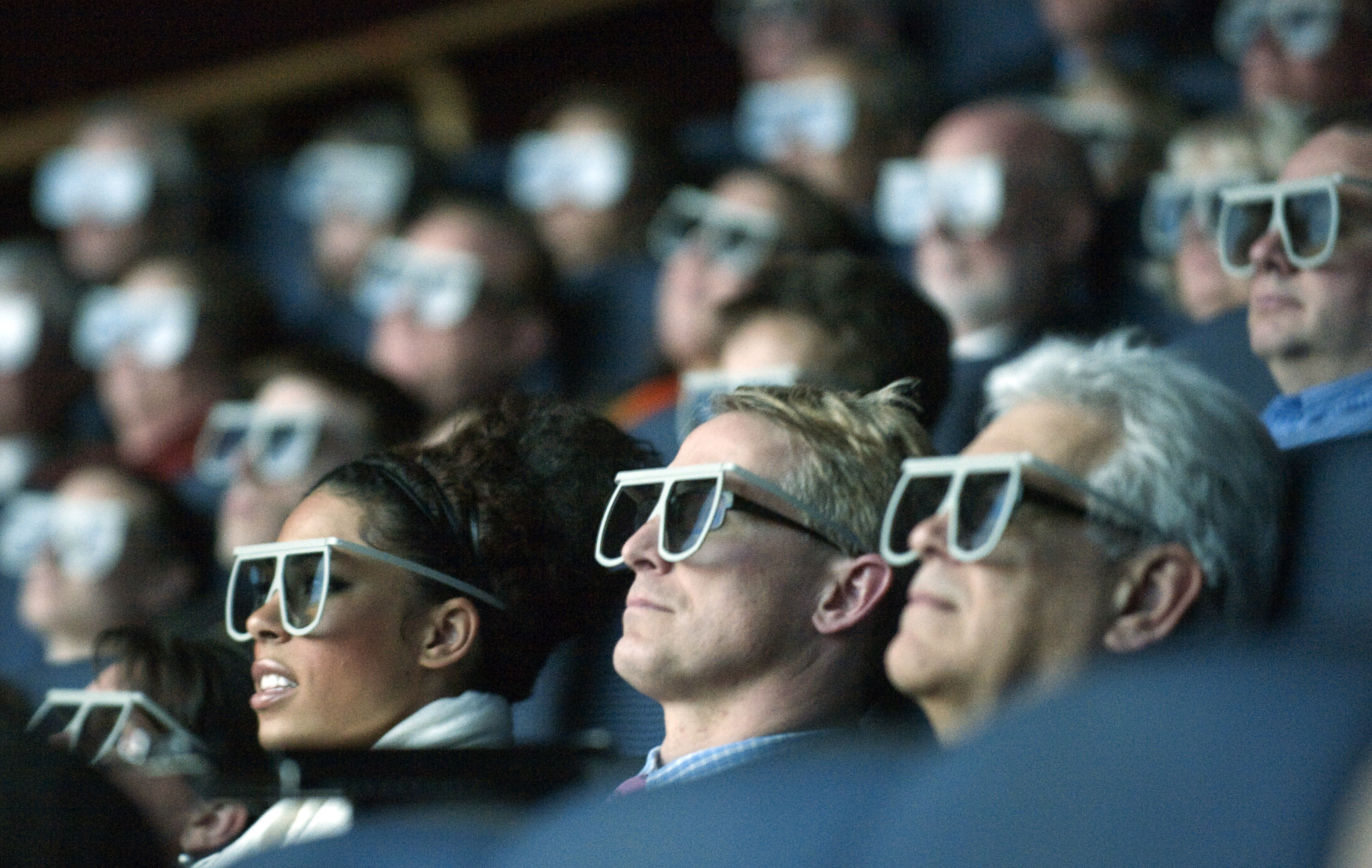 An audience of movie watchers wearing 3D glasses.