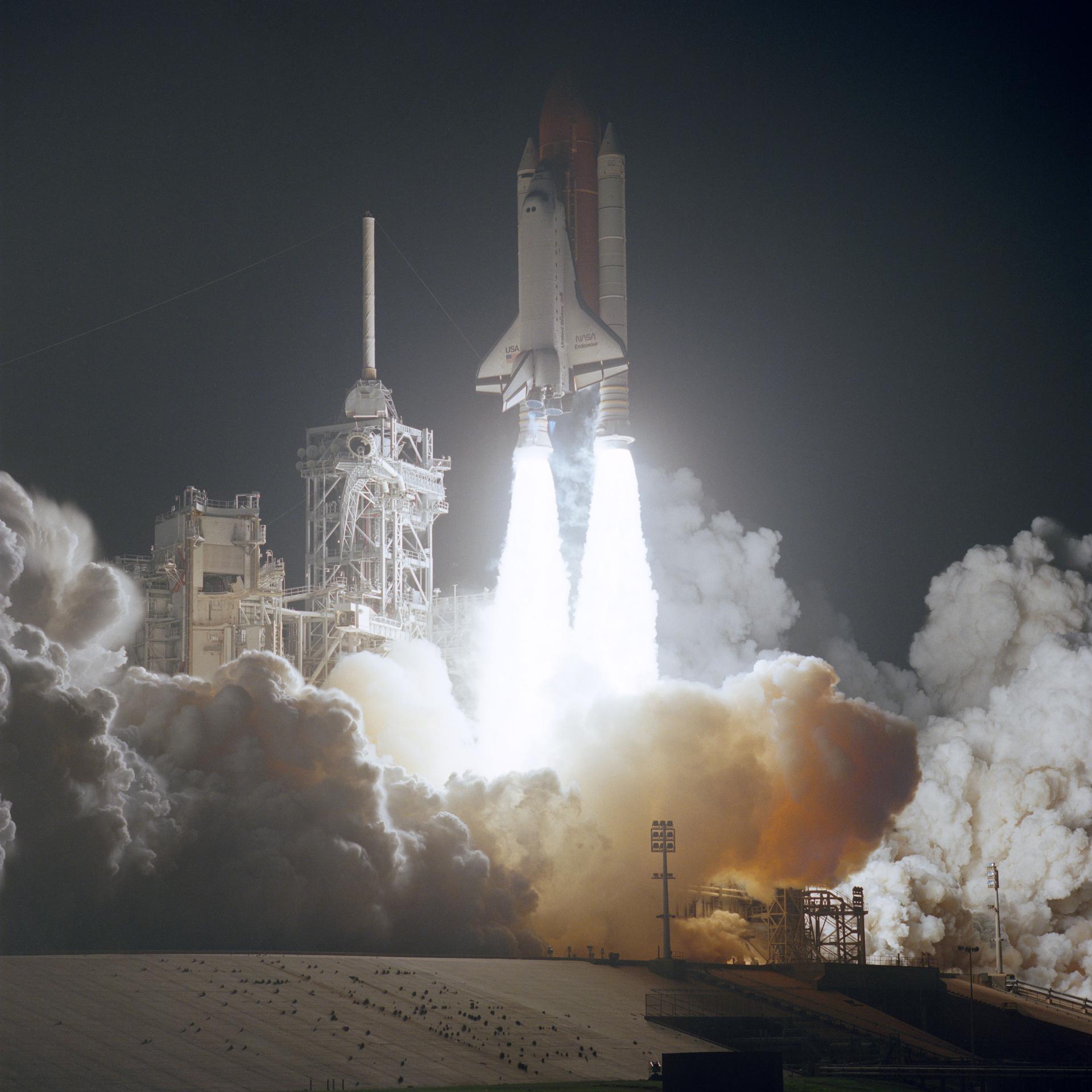 The space shuttle roars off the launchpad.