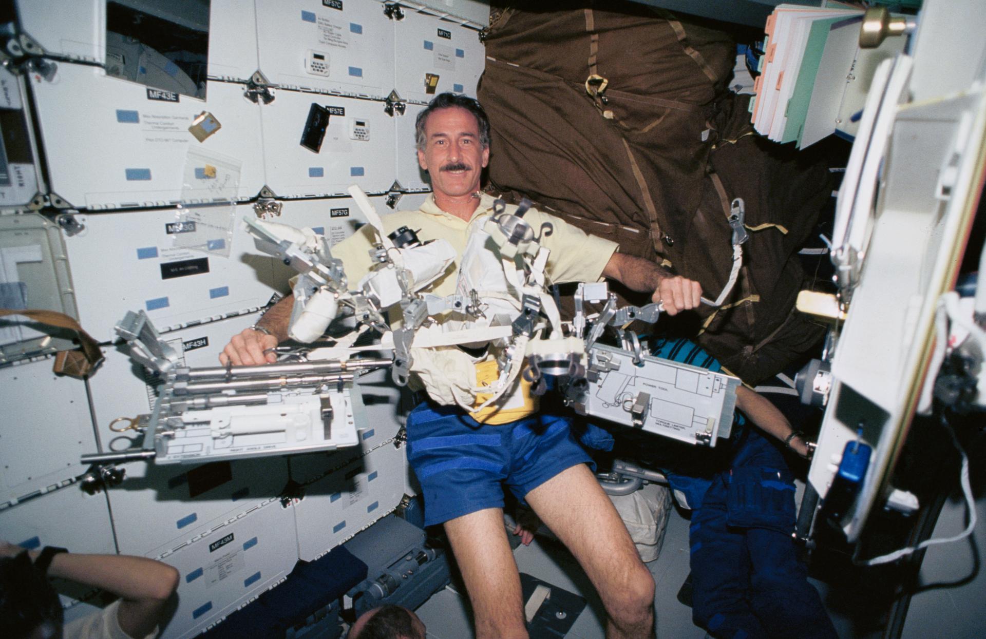 An astronaut floats in the space shuttle crew cabin with numerous tools.