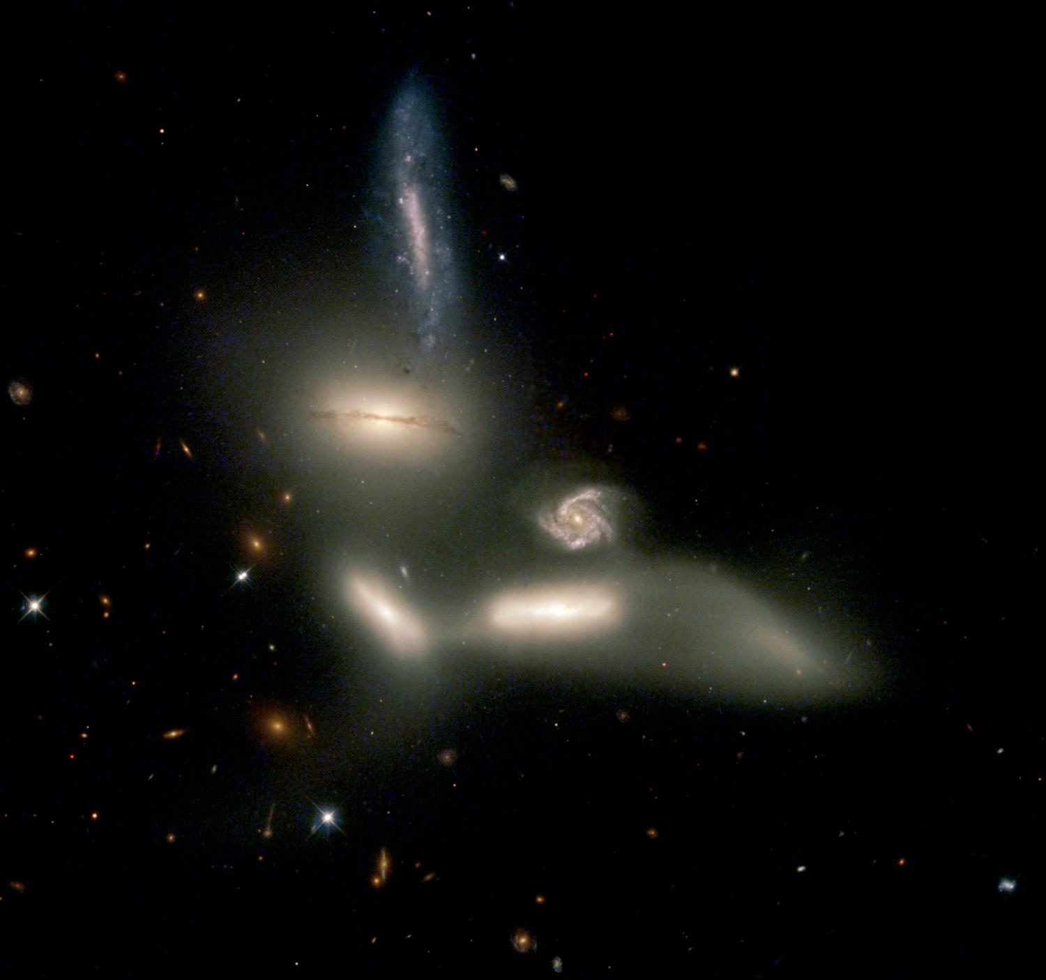 Group of galaxies bunching together with distant galaxies far away in the background.