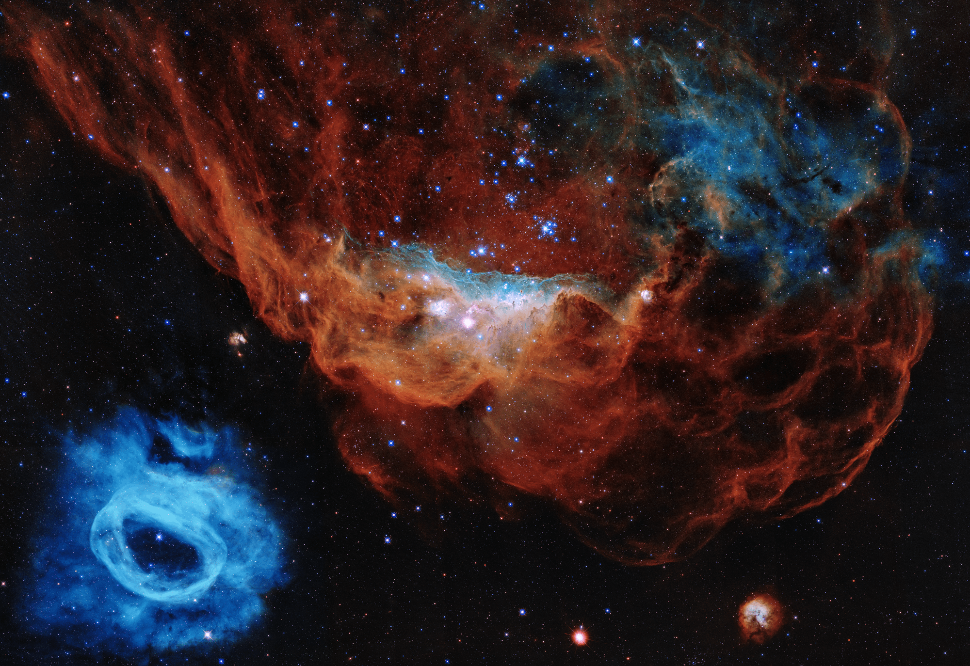 A large, red, nebula of dust and gas at the top right portion of the image with a small blue bubble at the bottom left.