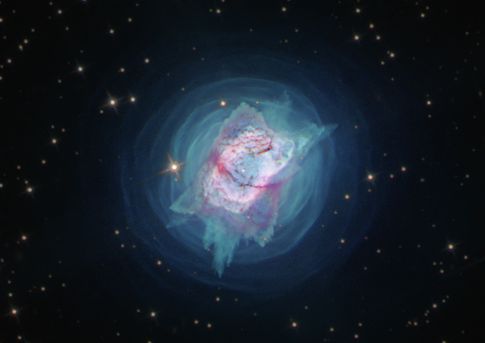 Bright blue cloud of dust and gas with bits of purple gas surrounding it the large glob of gas in the center.